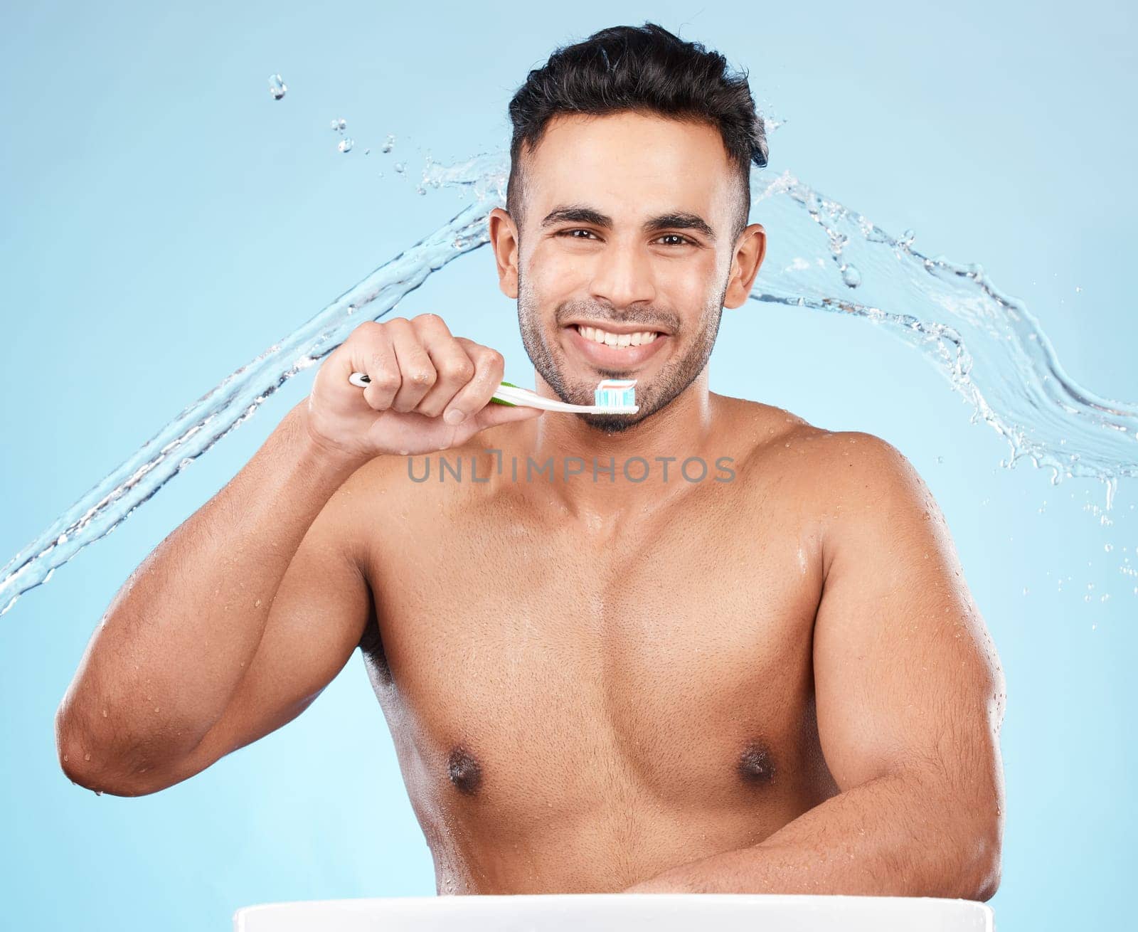 Teeth, dental care and water splash, man with toothbrush and toothpaste on blue background with smile on face. Morning routine, healthcare and fresh studio portrait of model in India brushing teeth