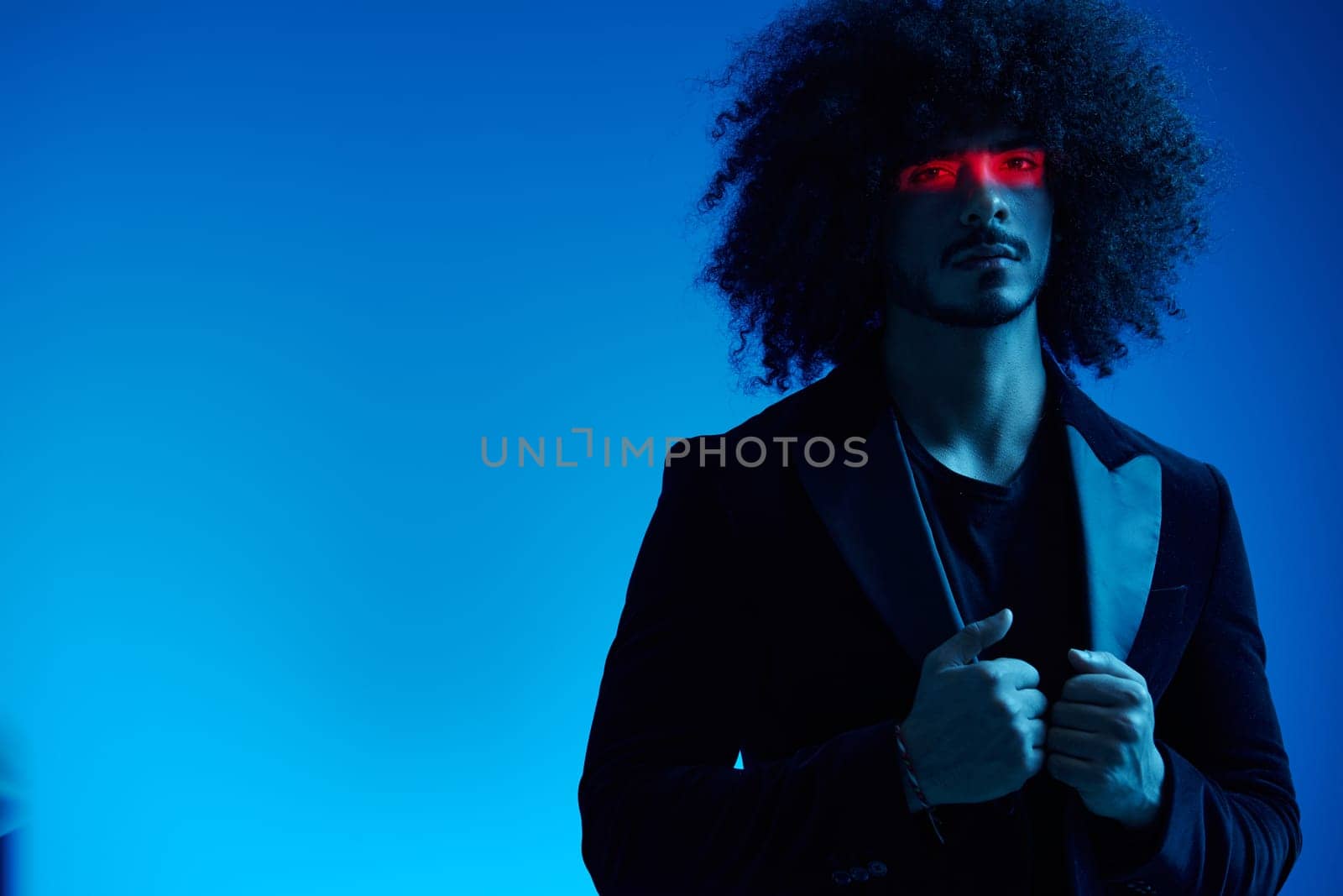 Fashion portrait of a man with curly hair on a blue background with a red stripe of light, multicolored light, trendy, modern concept. High quality photo