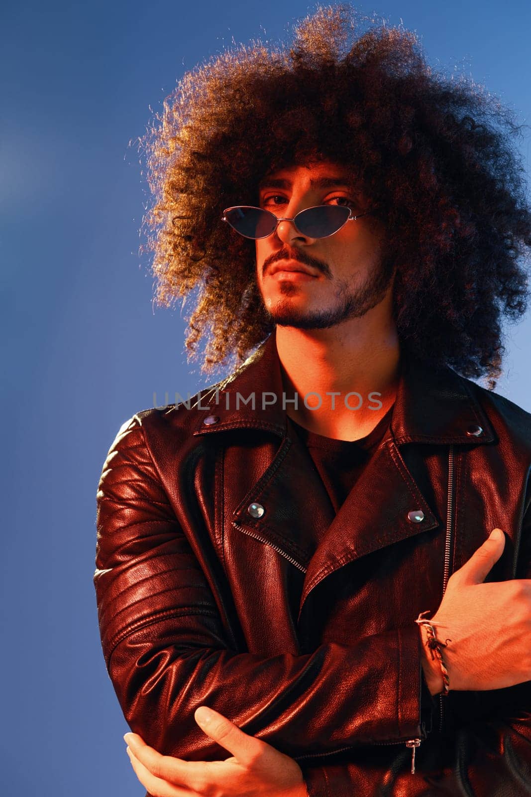 Portrait of a stylish man with curly hair on a blue background multinational, colored light, trendy glasses, modern concept. High quality photo