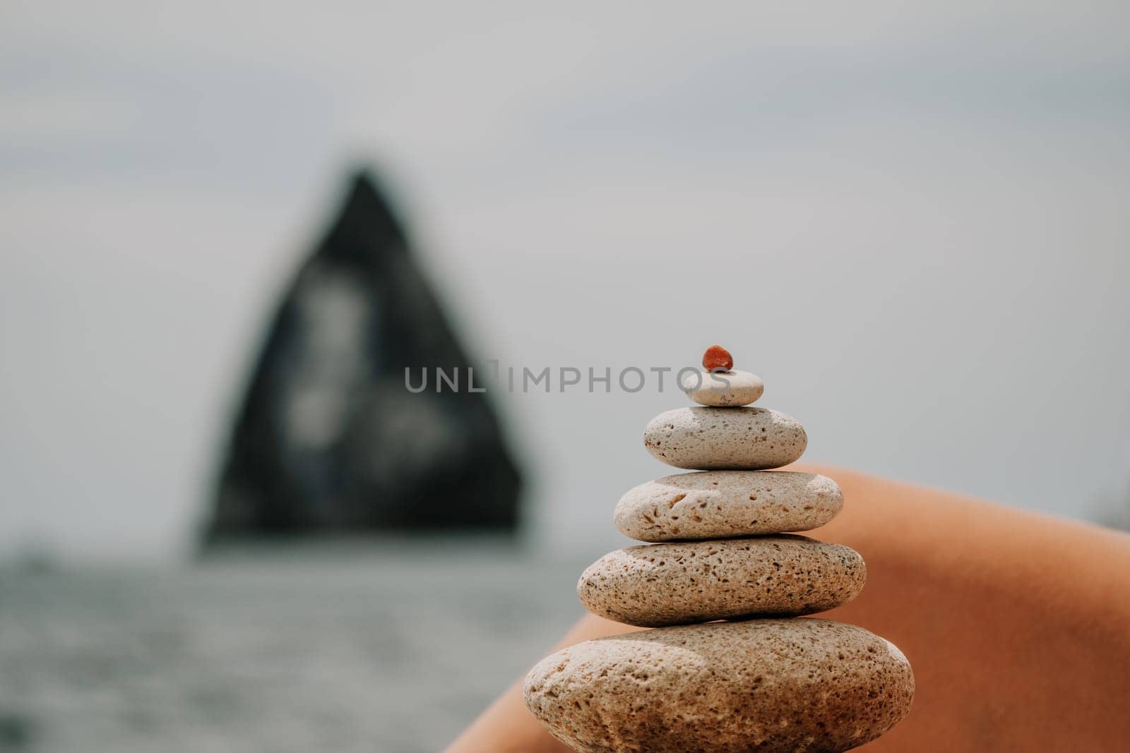 Woman bilds stones pyramid on the seashore on a sunny day on the blue sea background. Happy holidays. Pebble beach, calm sea, travel destination. Concept of happy vacation on the sea, meditation, spa