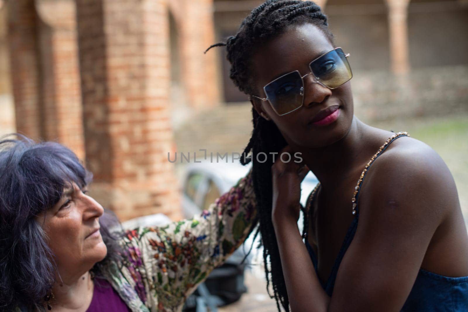 Happy young woman feeling confident in her style. Fashionable woman wearing sunglasses and braided hairstyle outdoors. Tourist traveling italian old village.