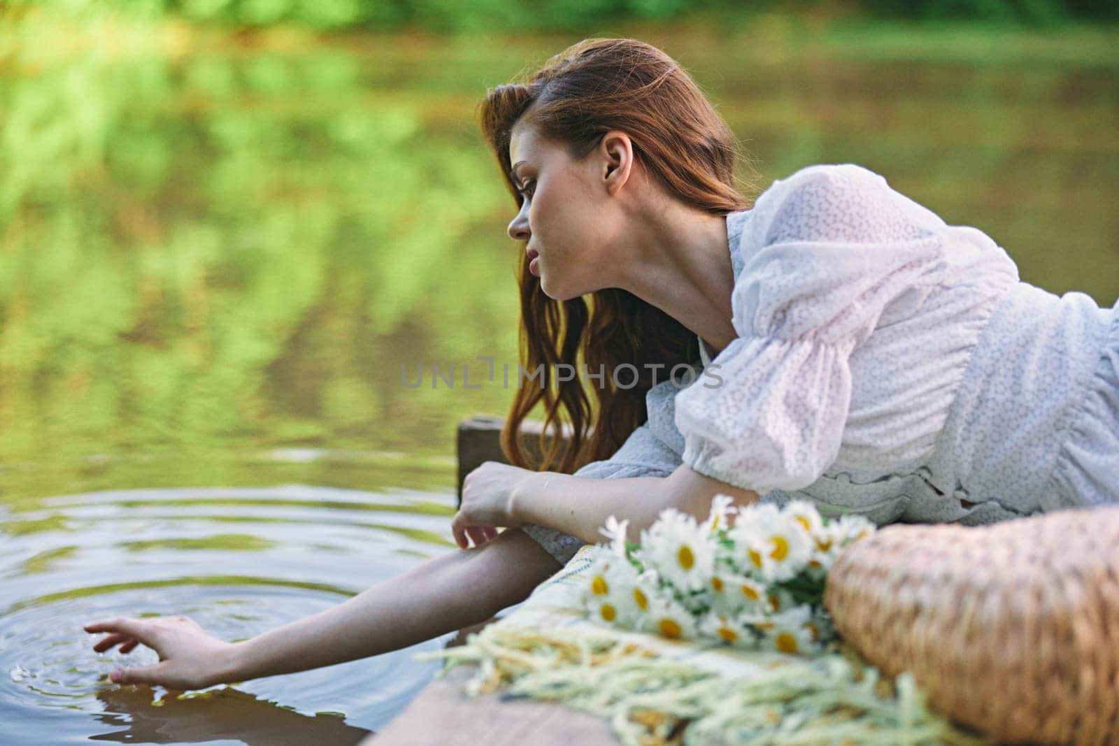 a woman in a light dress lying on a pier by the lake touches the water. High quality photo