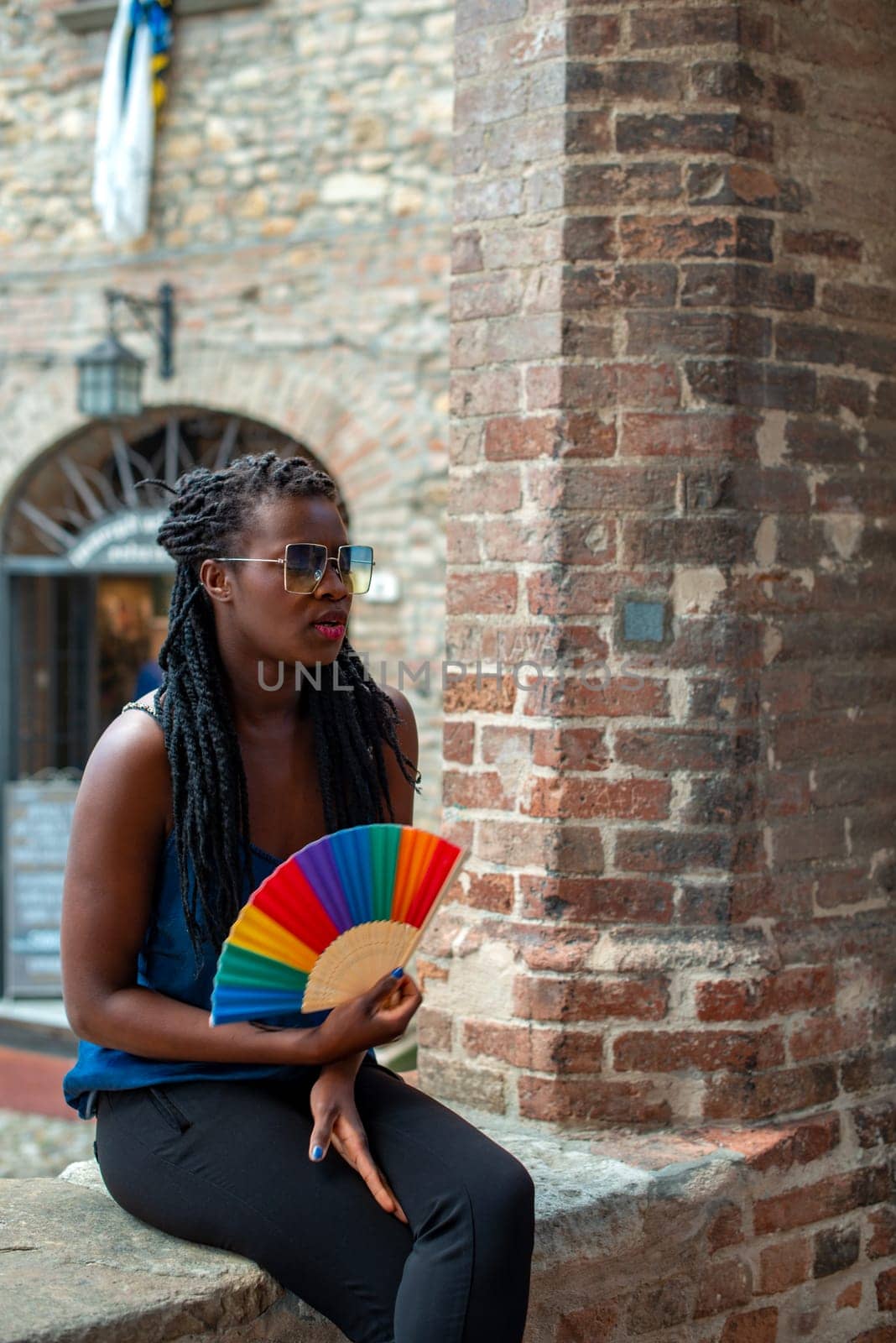 Young black confident african female model dreadlocks braids style, looking at camera holding rainbow pride fold fan, strong look.