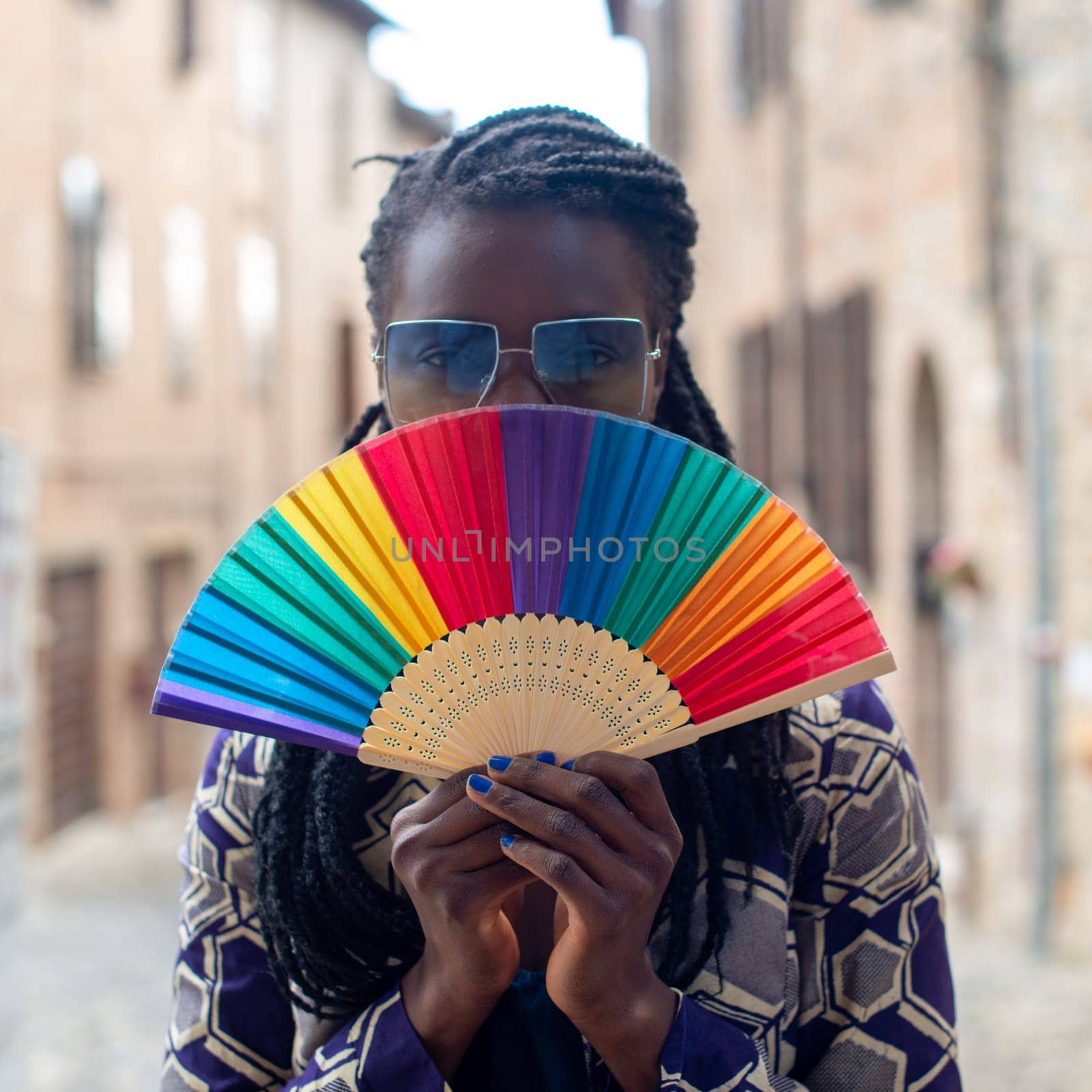 Young black confident african female model dreadlocks braids style, looking at camera holding rainbow pride fold fan, strong look, summertime.