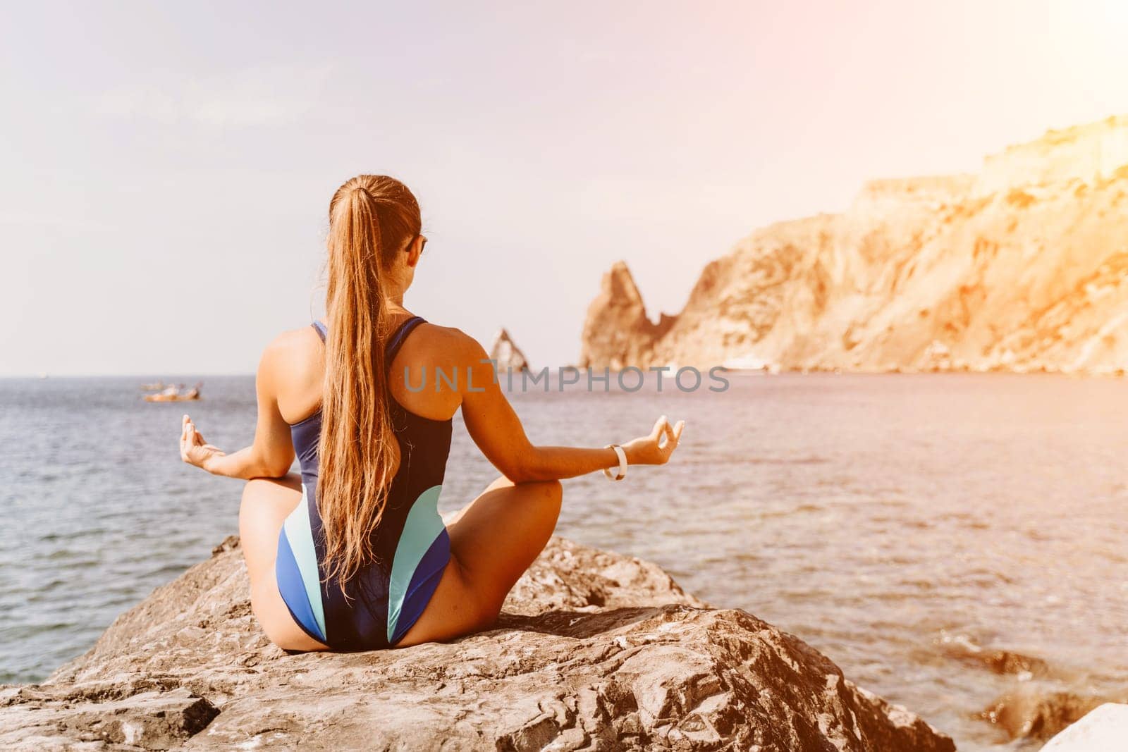 Yoga on the beach. A happy woman meditating in a yoga pose on the beach, surrounded by the ocean and rock mountains, promoting a healthy lifestyle outdoors in nature, and inspiring fitness concept