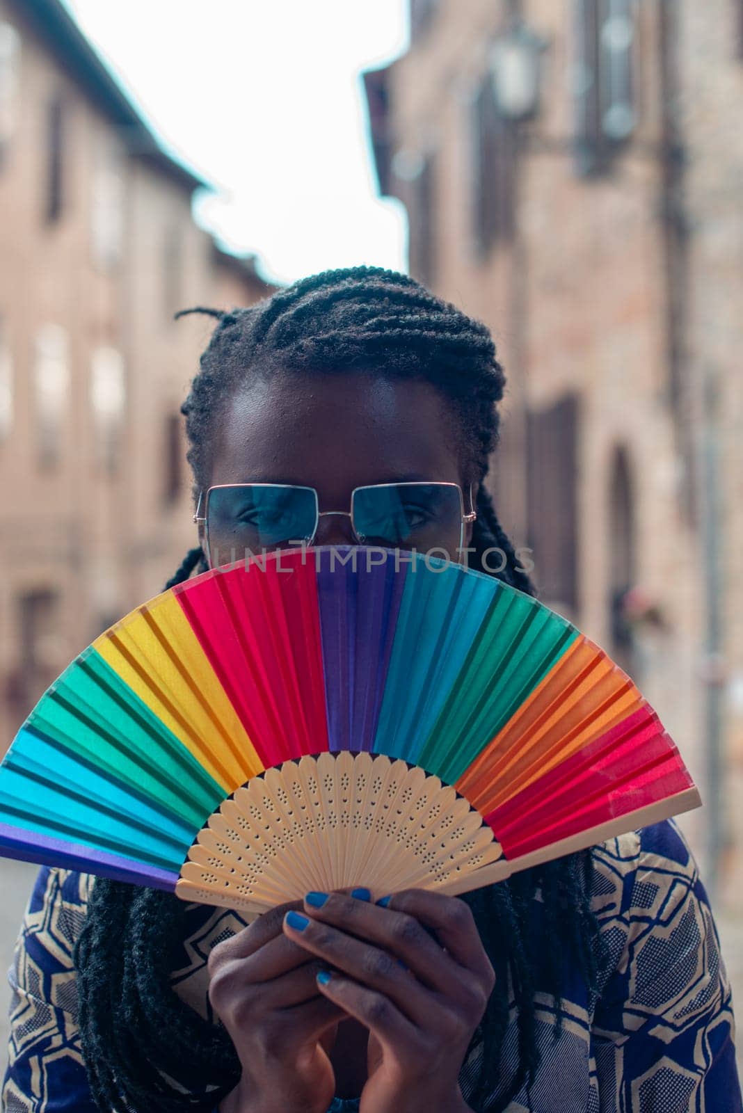 Young black confident african female model dreadlocks braids style, looking at camera holding rainbow pride fold fan, strong look, summertime.