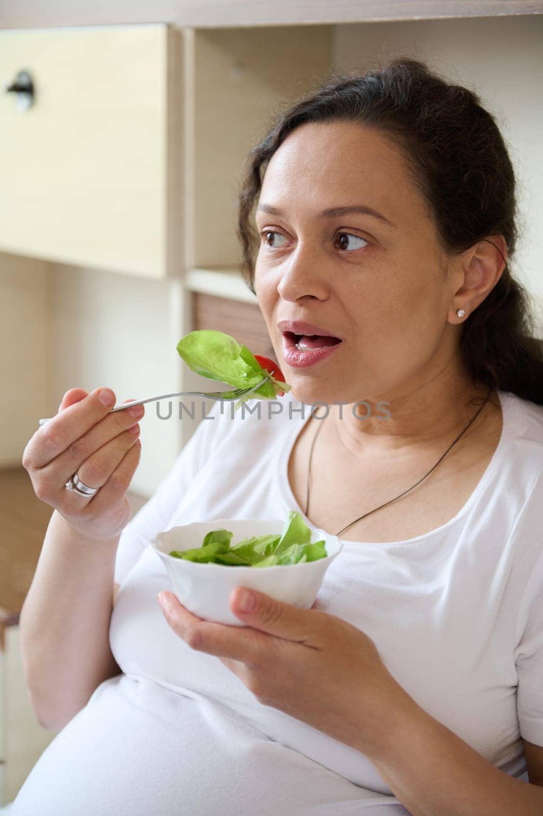 Close up portrait of a beautiful conscious adult pregnant woman, eating fresh salad from organic raw vegetables and greens. Pregnancy and healthy organic nutrition. Concept of expectation and health.