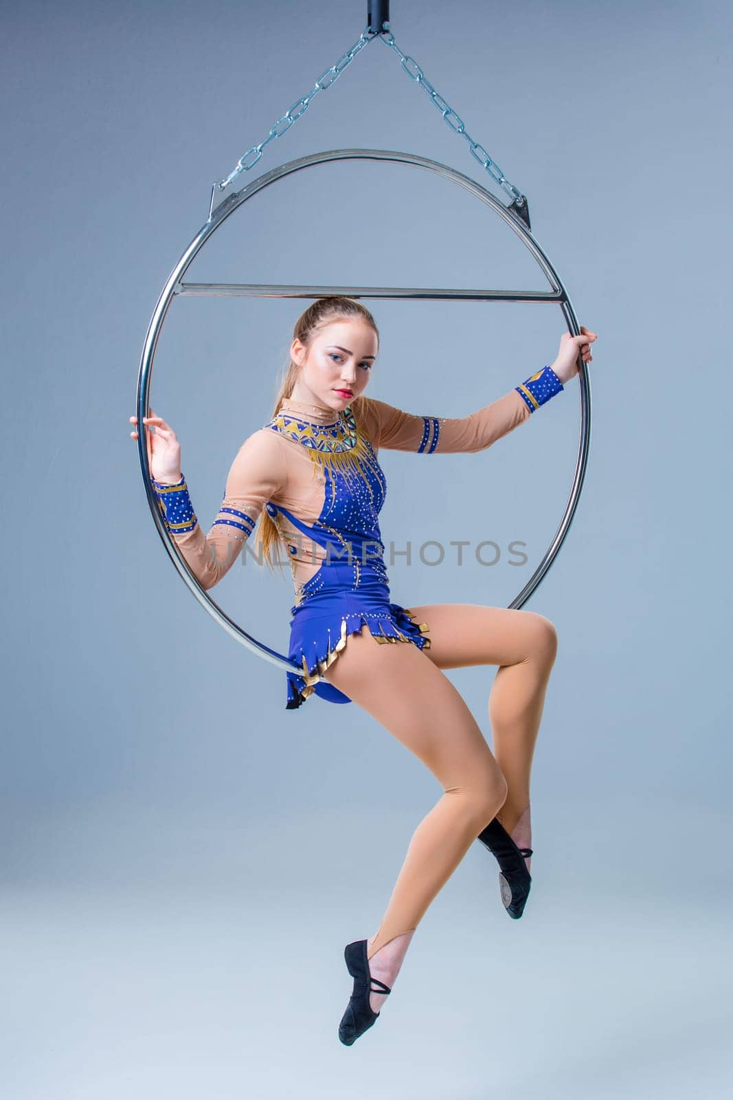 Young woman hanging in aerial ring on a blue background. The girl in a blue dancing suit