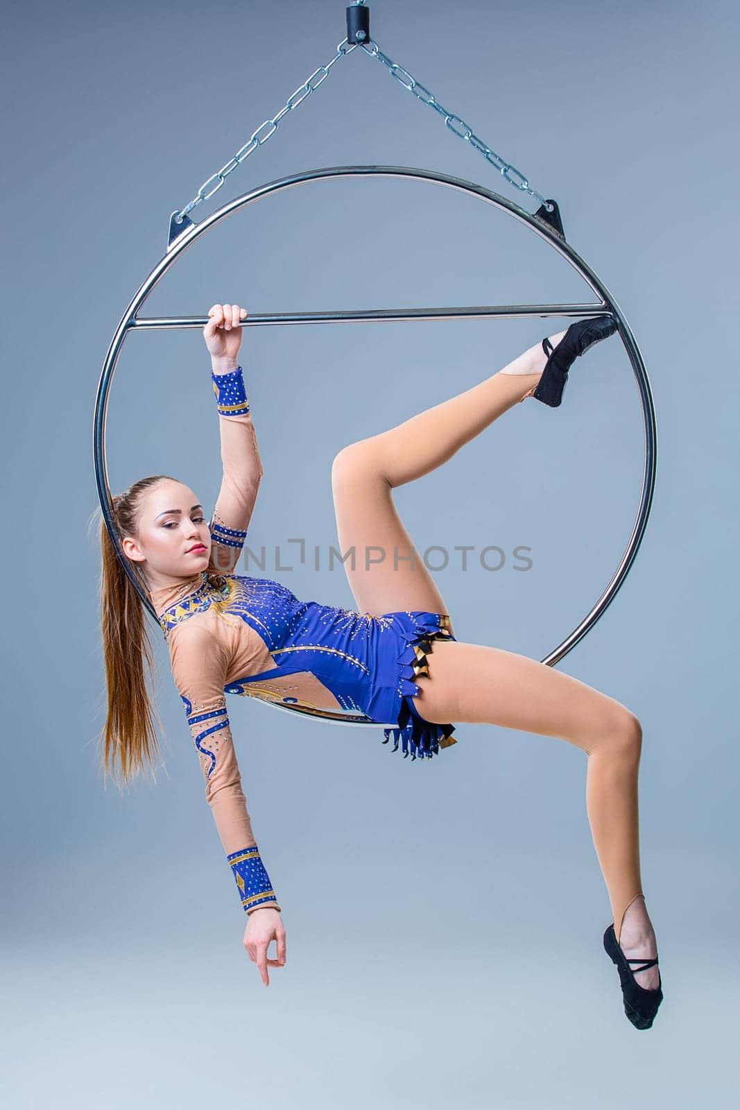 Cute artistic gymnast exercising with hanging hoop on a blue background