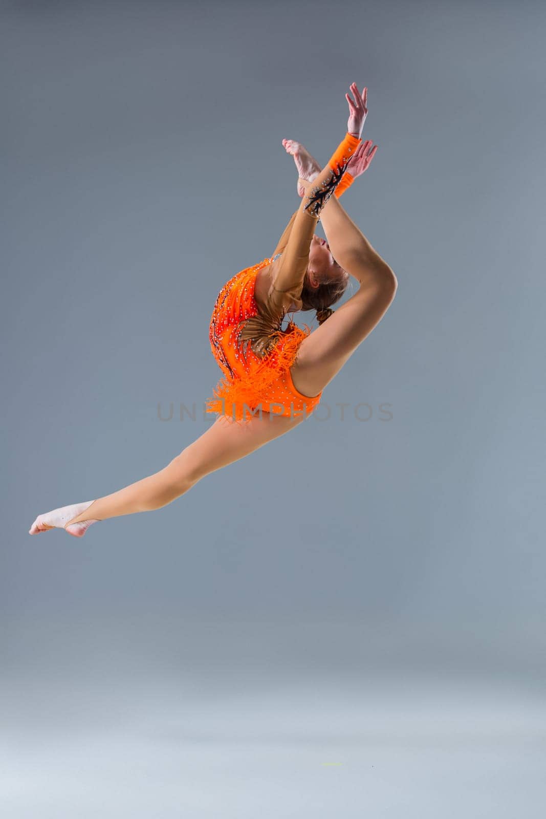 Young beautiful girl doing gymnastick jump on a blue background. The girl in the orange dancing suit