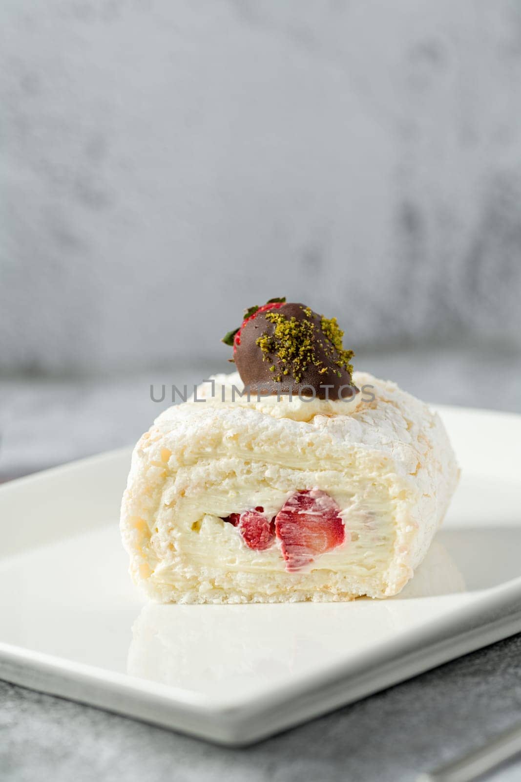 Strawberry roll cake with tea next to it on stone table by Sonat