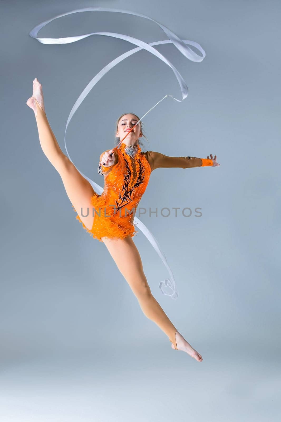 Young gymnast on a white background. Sporting exercises with ribbon. Aerobics. Flexibility. Plastic study. Twine