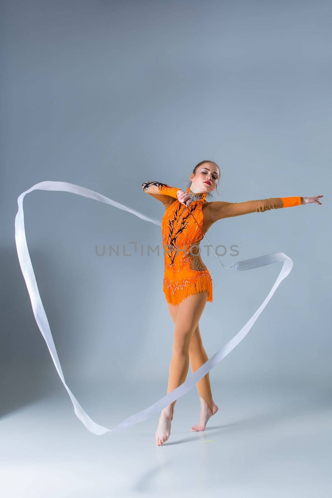 beautiful Caucasian girl gymnast with white ribbon on a blue background