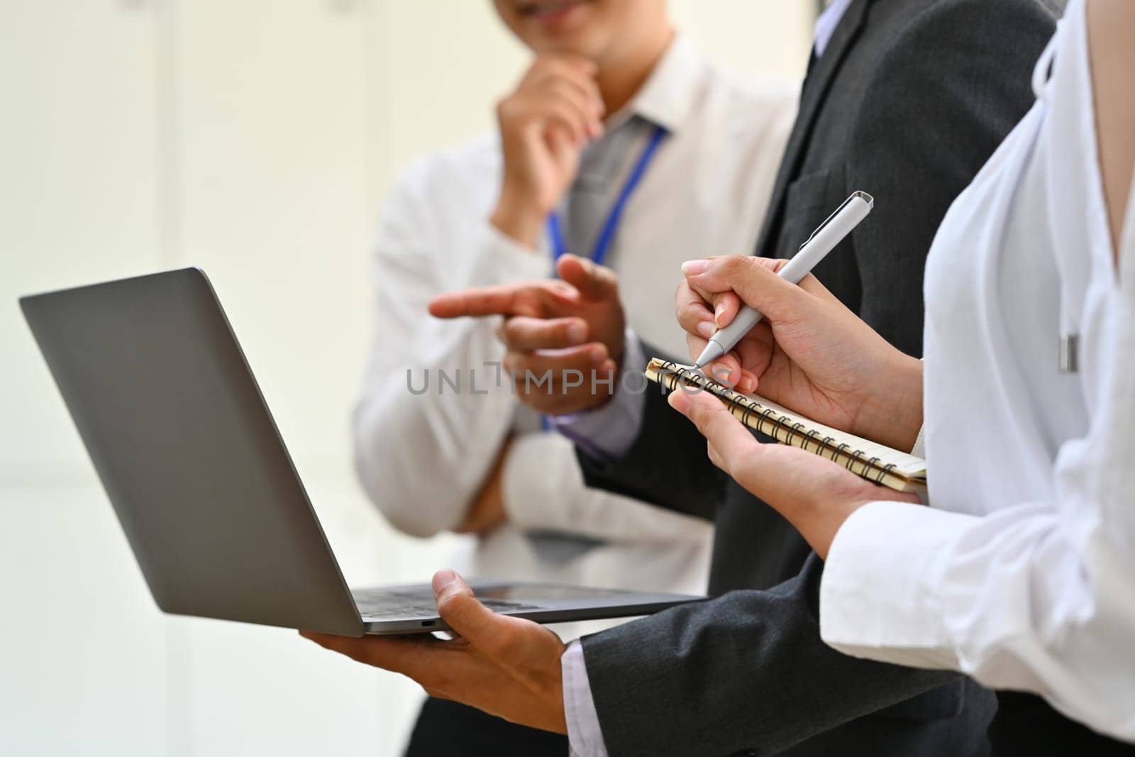 Businesspeople analyzing statistics data online on laptop screen while standing in meeting room.