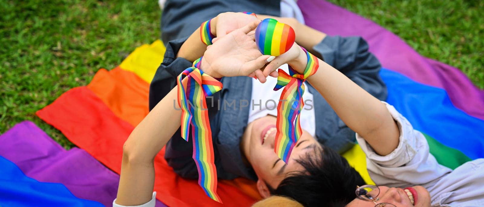Young people lying on green grass with LGBTQ pride flag, supporting LGBTQ community and equality social by prathanchorruangsak