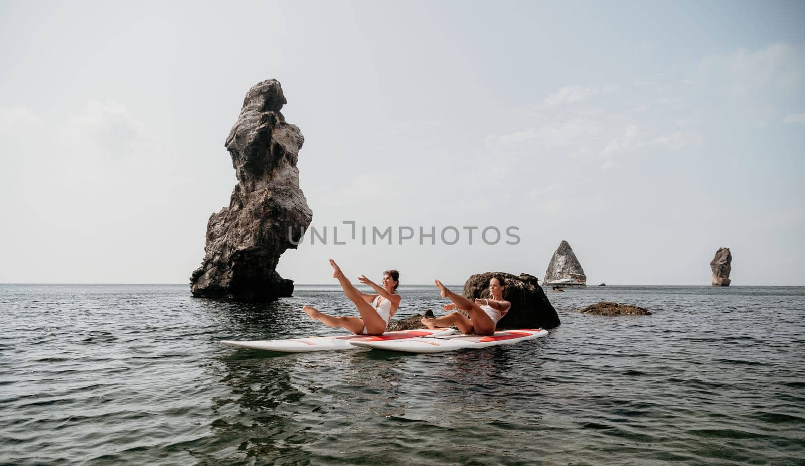 Woman sup yoga. Middle age sporty woman practising yoga pilates on paddle sup surfboard. Female stretching doing workout on sea water. Modern individual hipster outdoor summer sport activity