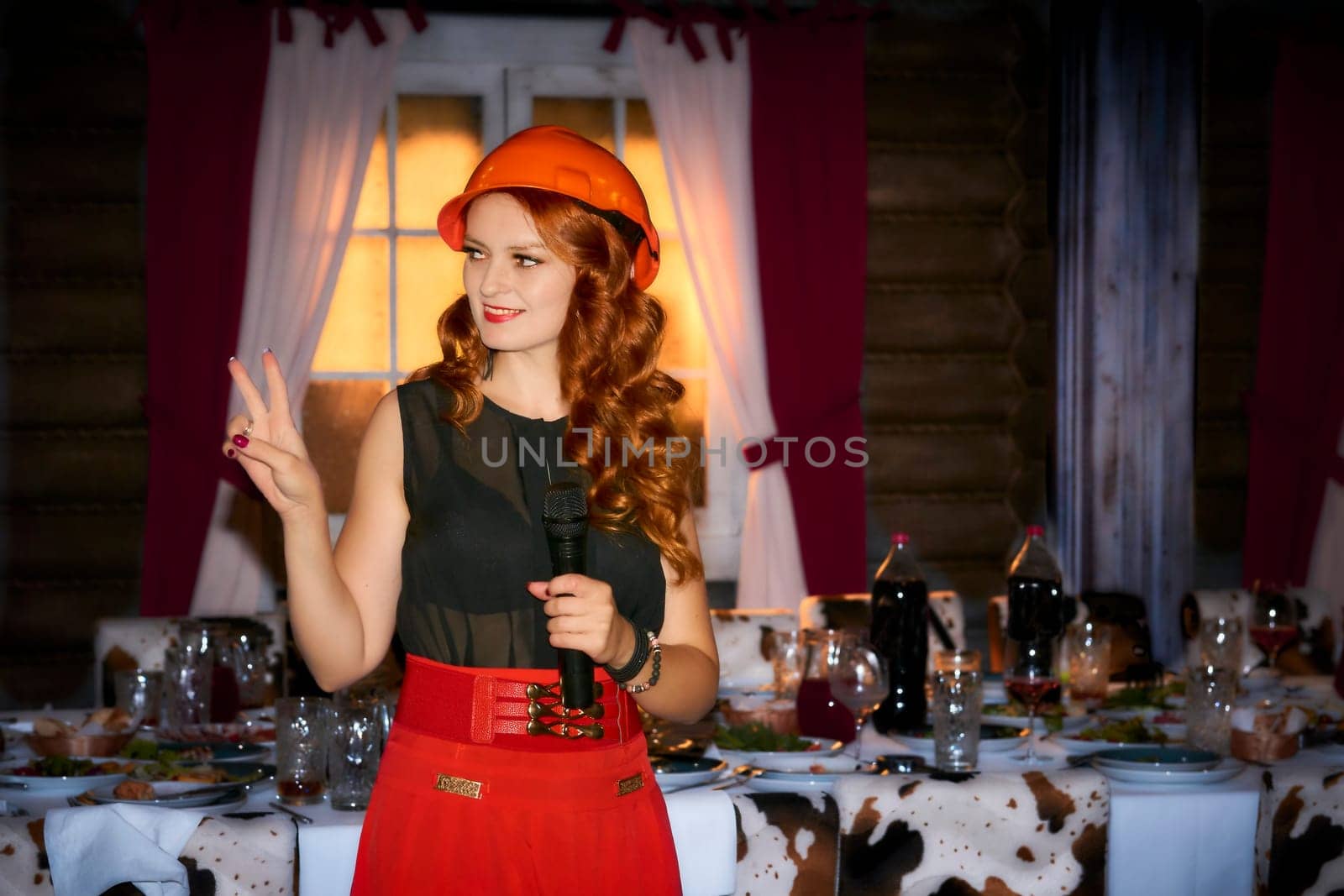 Charming presenter in a red protective construction helmet at a festively table by jovani68