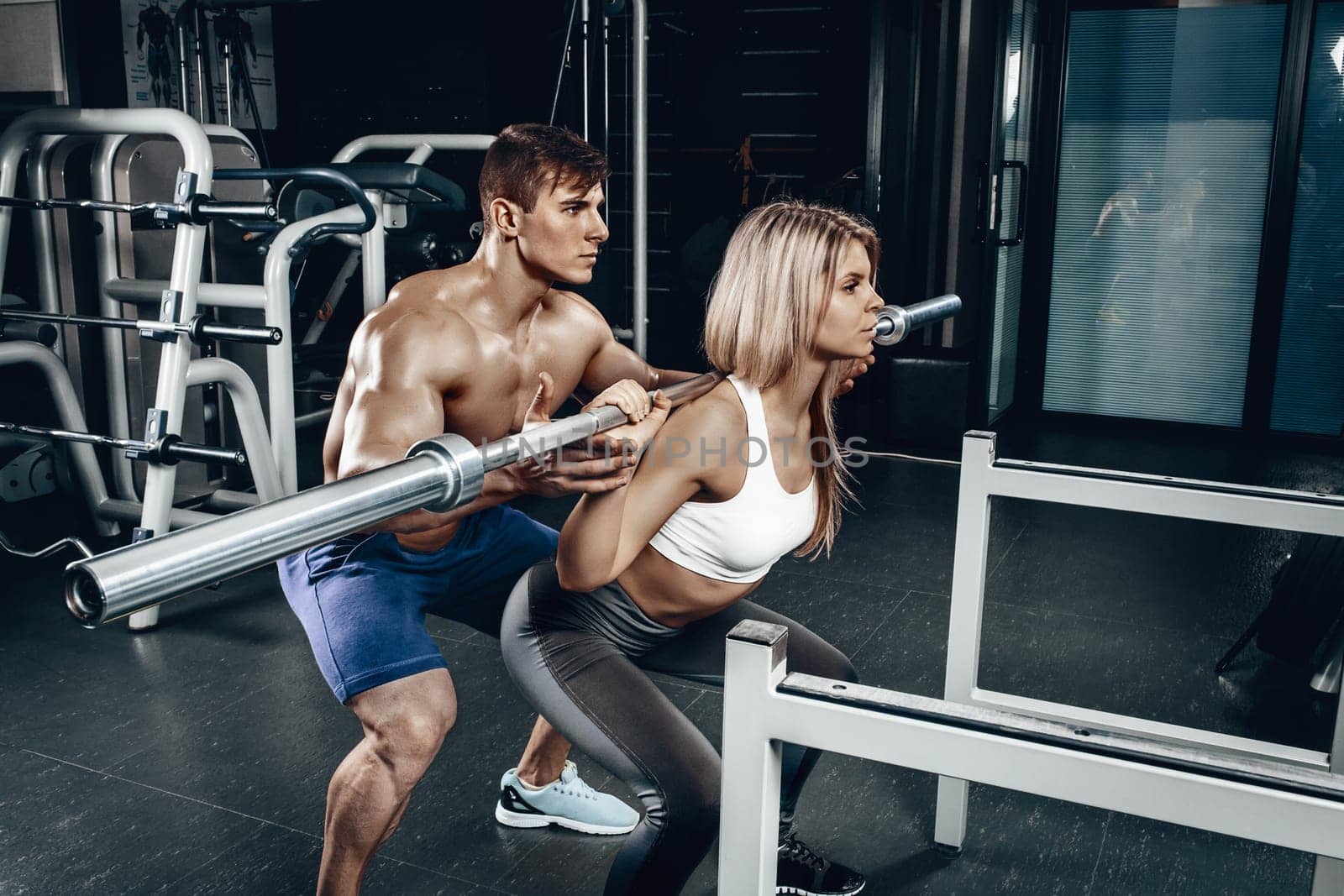 Personal trainer helping a young woman lift a barbell while working out in a gym by nazarovsergey