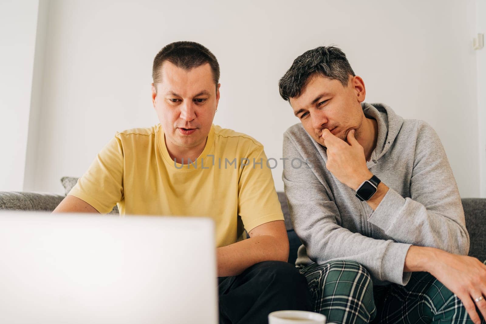 Two IT freelancer men typing in laptop working from home office. Two programmers sitting on couch doing code review. Distance learning online education and work.