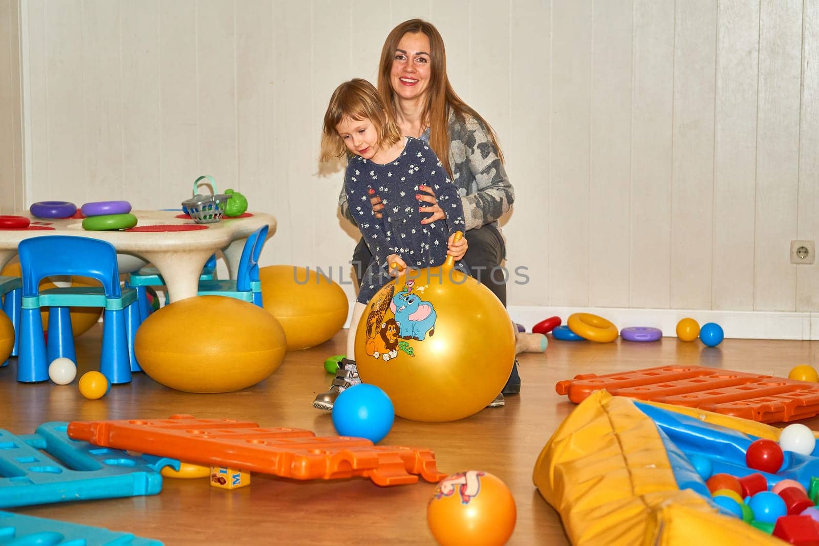 Pretty mother playing with cute daughter baby girl in playroom in kindergarten by jovani68