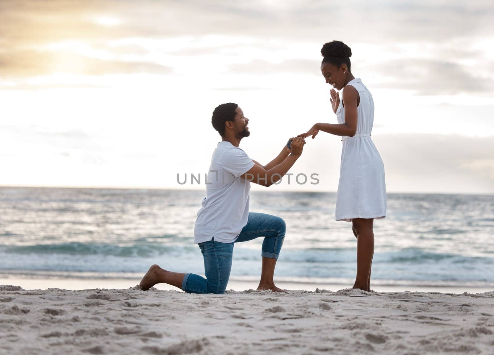 Love, beach and black couple with proposal, commitment and sunset with happiness, romance and holiday. Romantic, man or woman with engagement ring, asking and question with seaside vacation and smile.