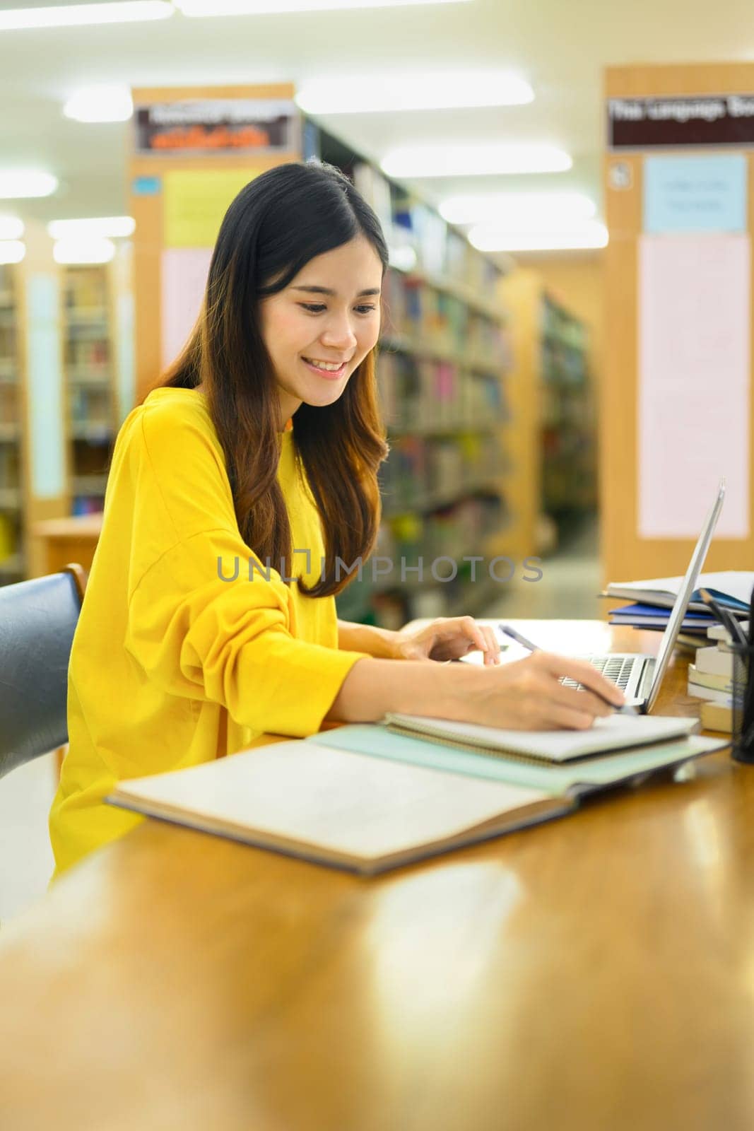 Portrait of asian female student doing class assignment and searching information on laptop in library. Education concept.
