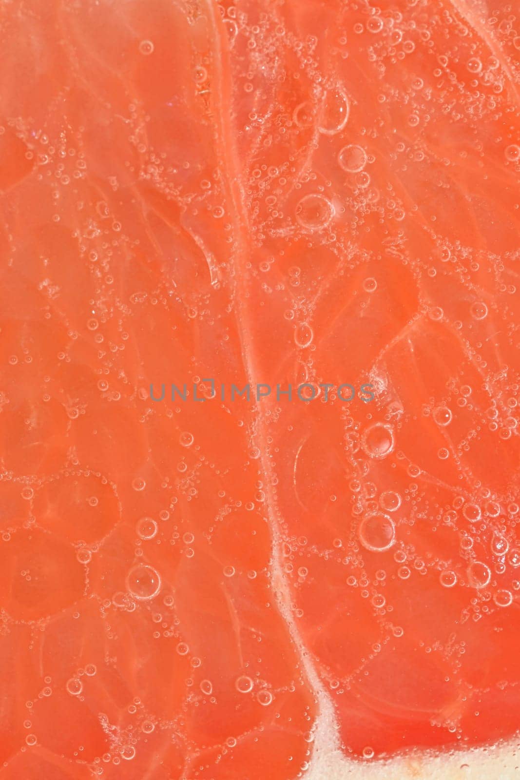 Slice of ripe grapefruit in water. Close-up of grapefruit in liquid with bubbles. Slice of ripe grapefruit in sparkling water. Macro image of fruit in carbonated water. Abstract and background