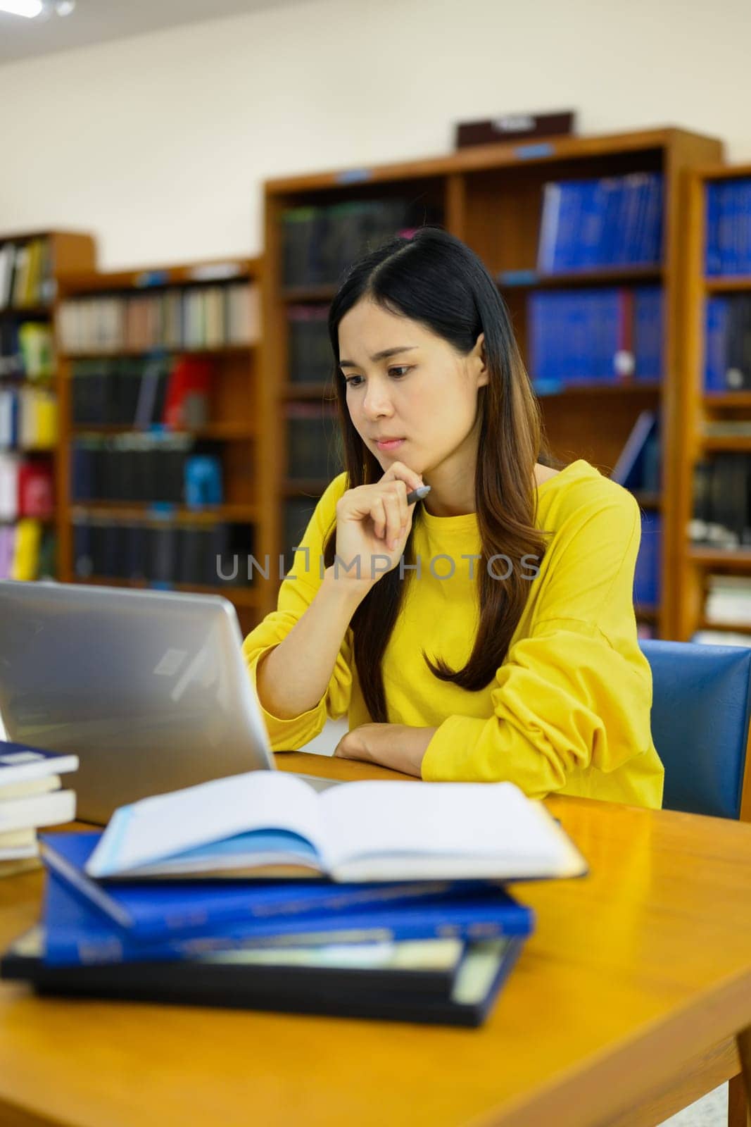 Focused female university student doing research on laptop, learning lessons, preparing for exams in library.