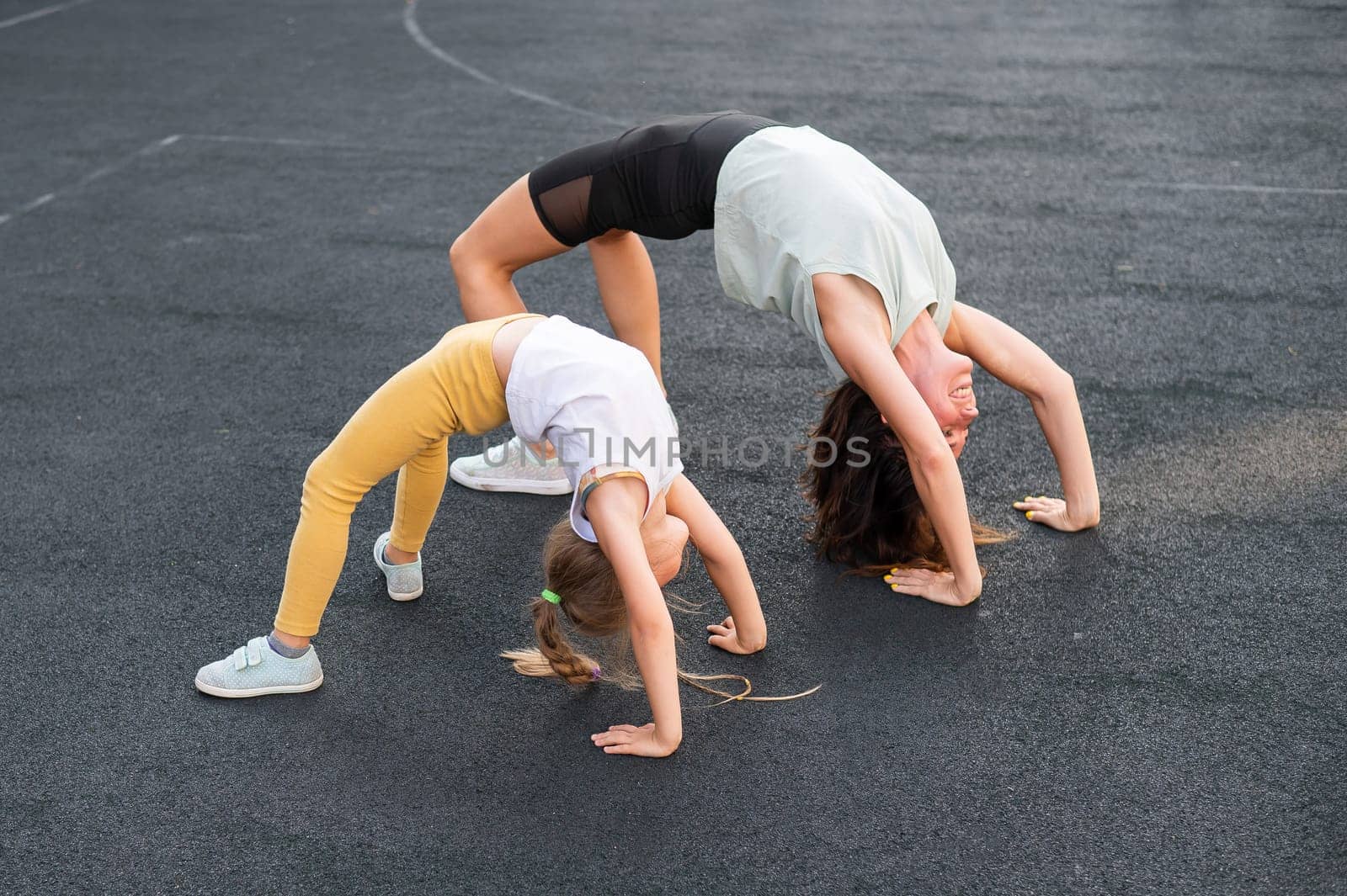 A little girl and her mom do a bridge exercise at the outdoor sports ground
