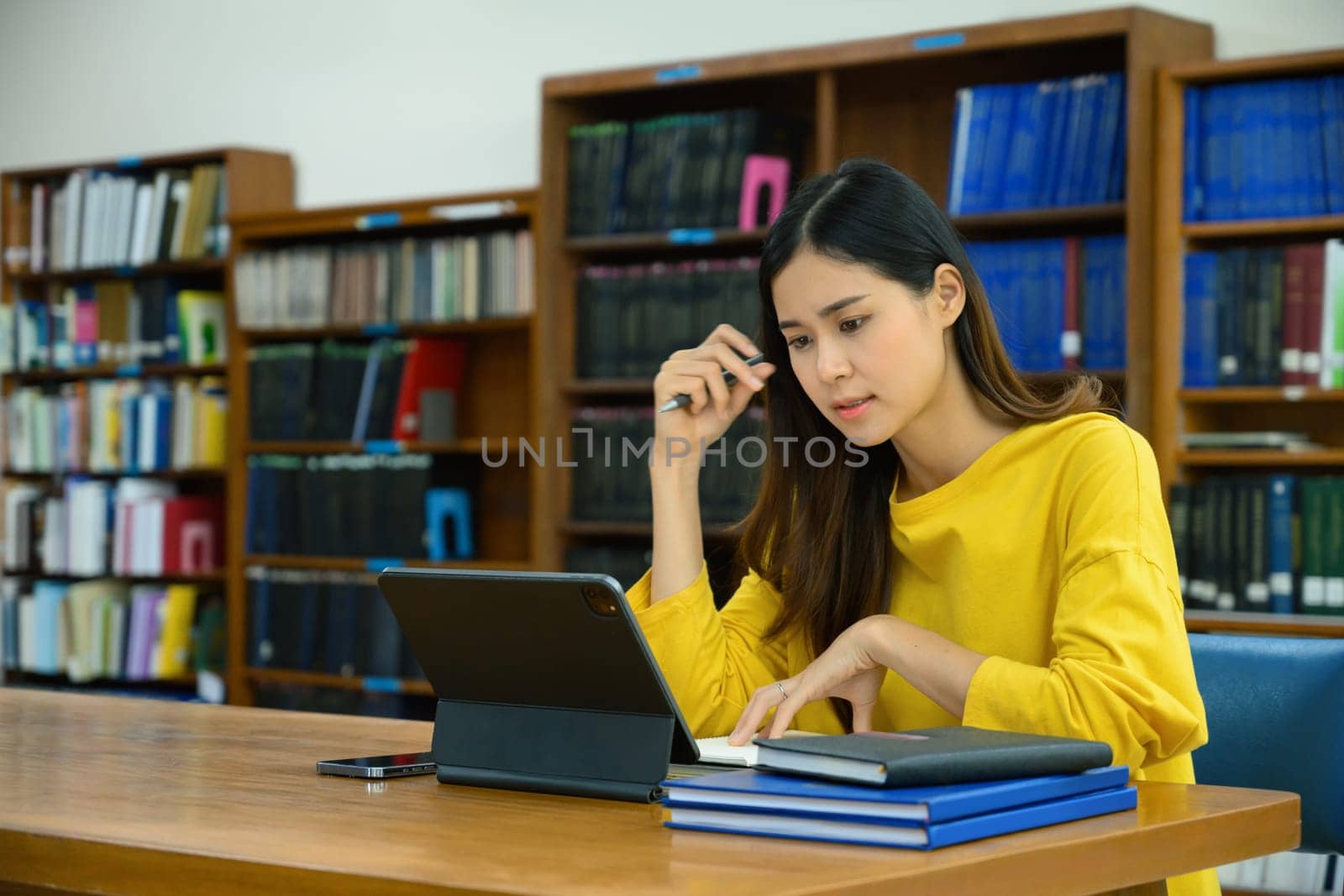 Concentrated female university student doing research on digital tablet, learning lessons, preparing for exams in library.