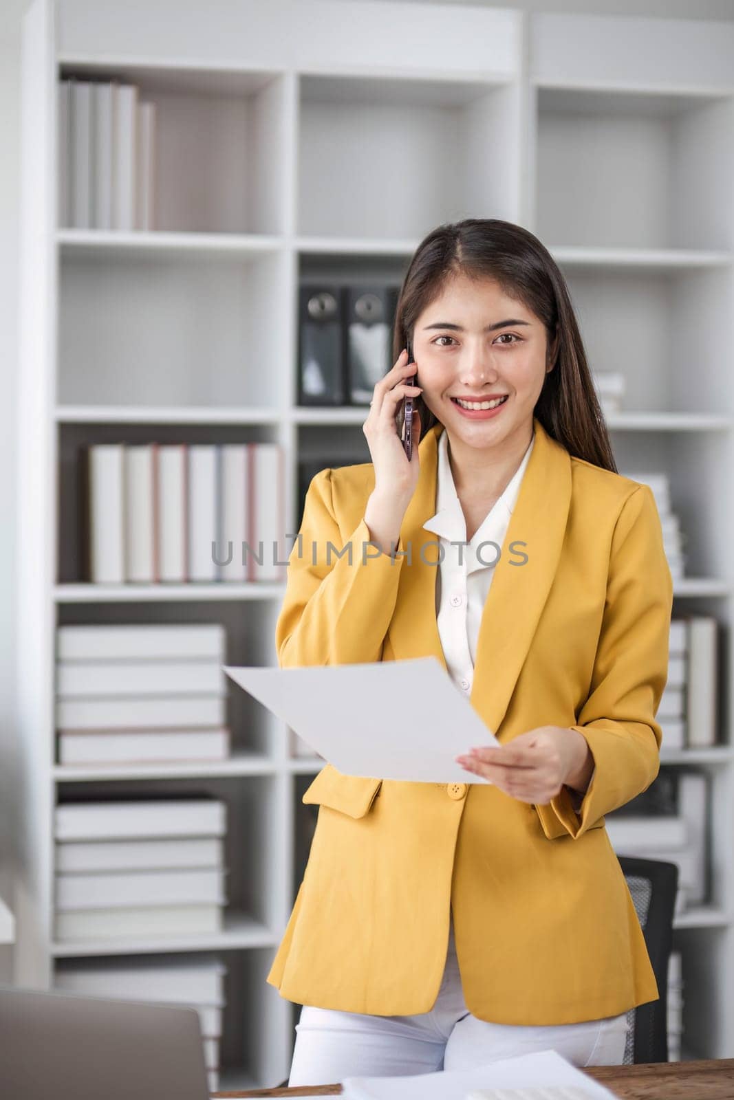 Young busy asian business woman talking on phone working in modern office. Asian businesswoman company sales client manager wearing suit making call on cellphone sitting at workplace...
