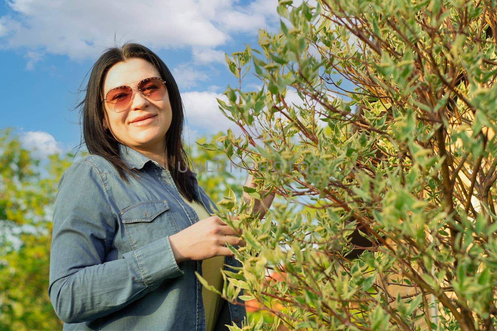 Camping. A beautiful girl in jeans and sunglasses, stands near a blooming green tree, smiles happily. Fresh air concept. Sunset.