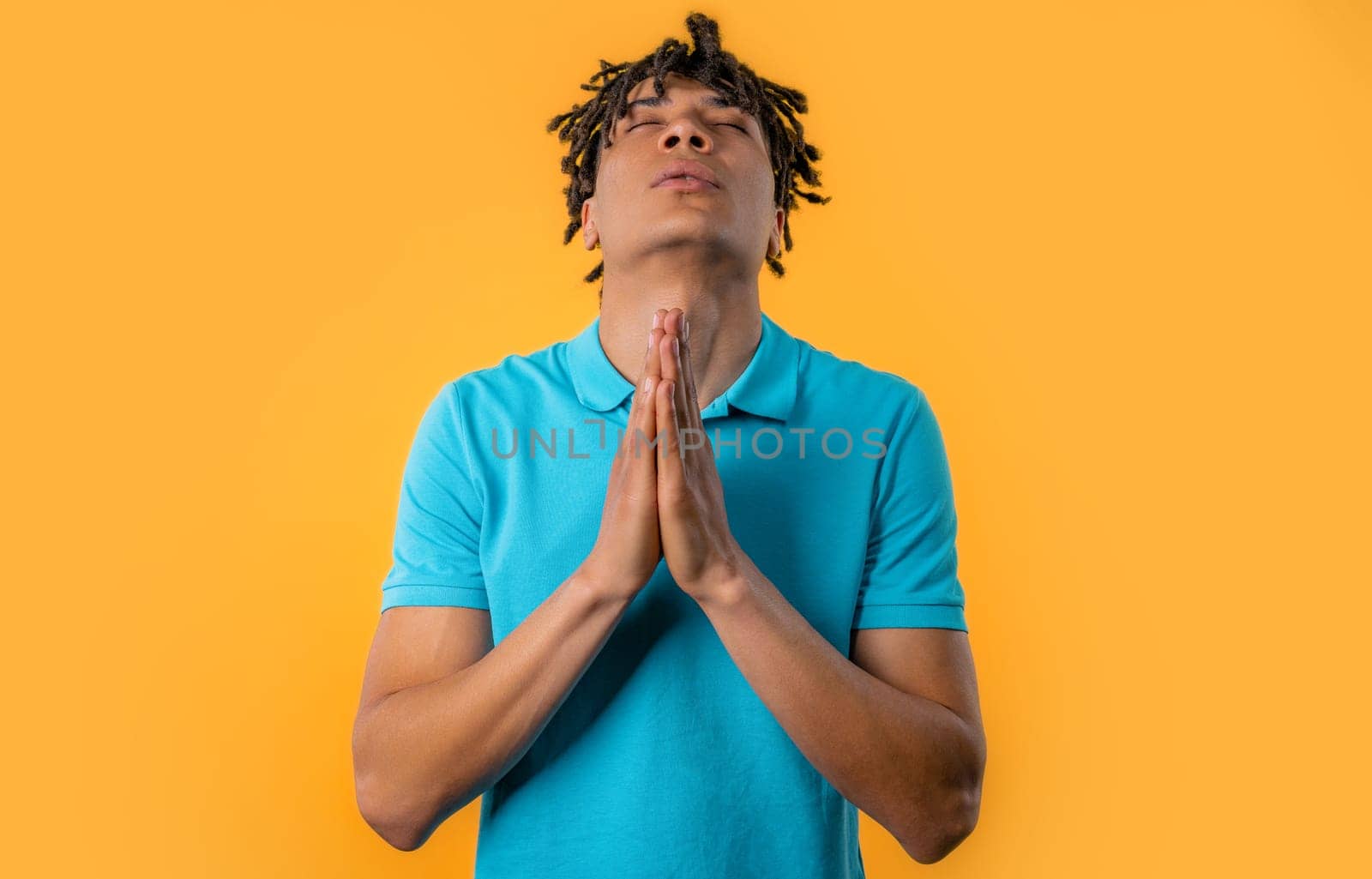 Young man praying with crossed fingers on yellow background. Guy begs someone satisfy desires, help with, prays for luck in exam. High quality