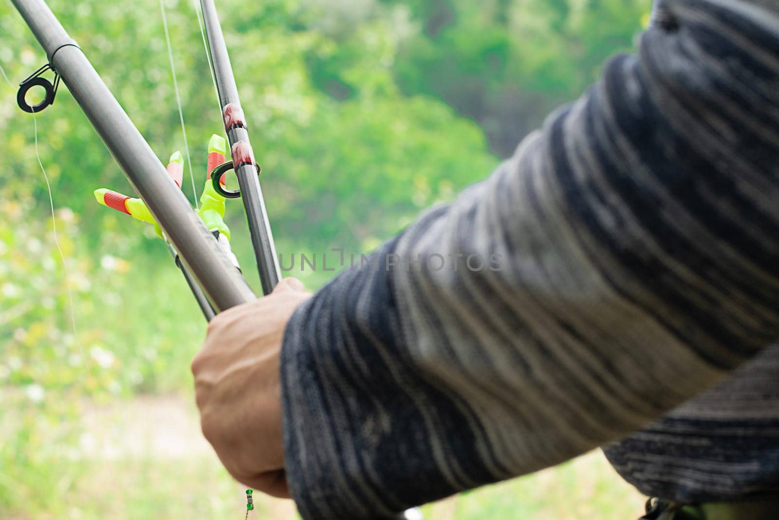 Fishing concept. A man holds two fishing rods in his hands on the background of the river. Getting ready to fish with a float rod. Close-up. Soft focus.