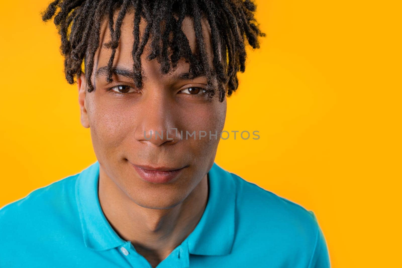 Portrait of friendly african man in blue t-shirt. Positive smiling guy on yellow. High quality photo