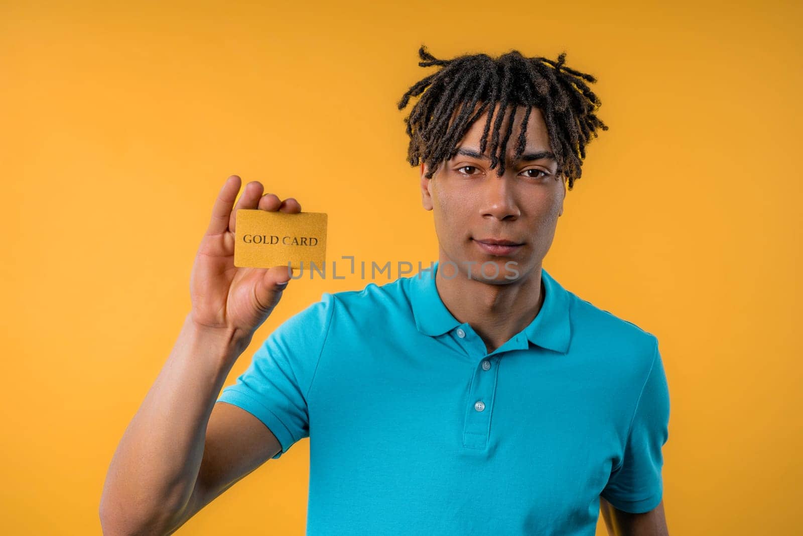 Successful handsome african american man showing unlimited gold credit card and look to camera yellow studio background. High quality photo