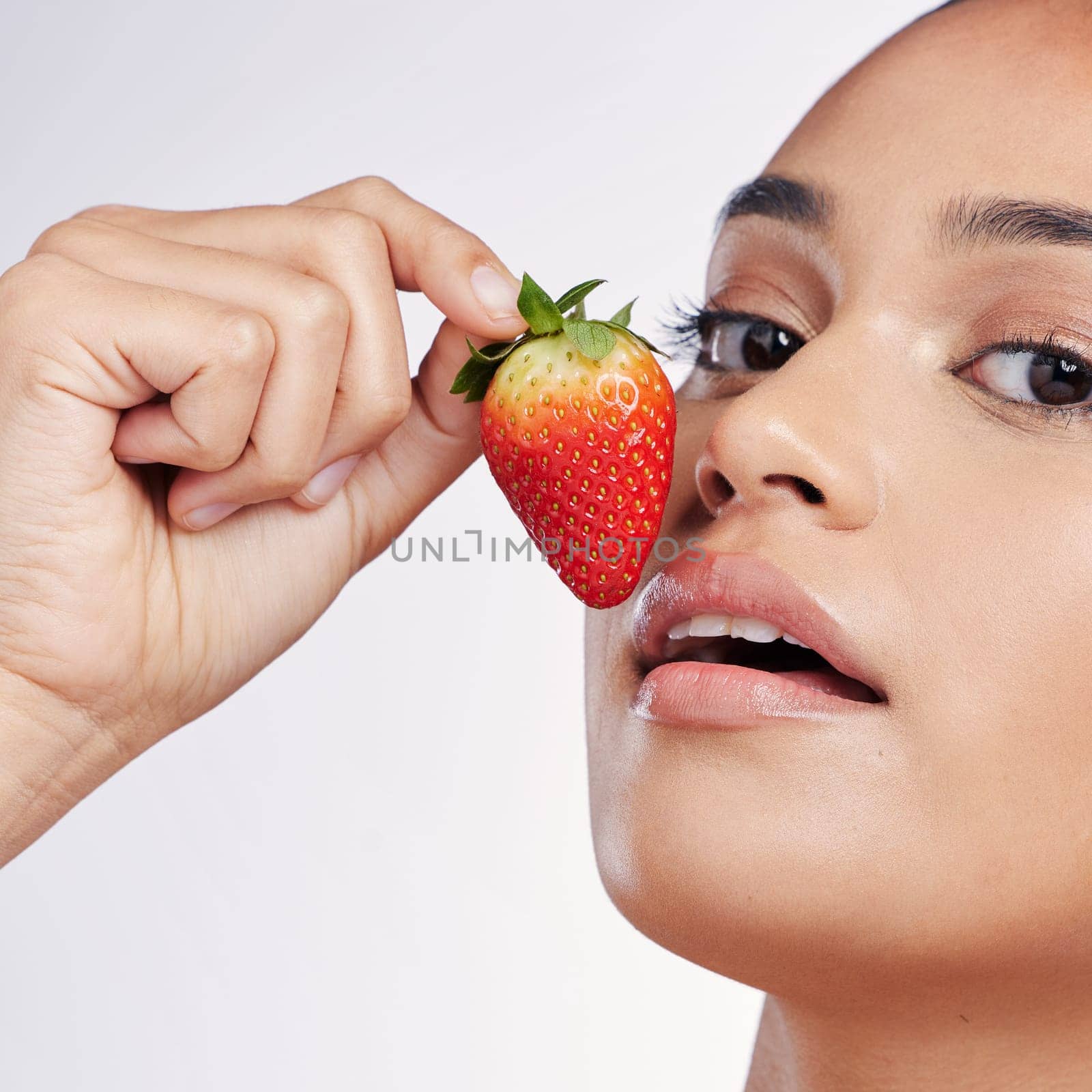 Face, lips and strawberry portrait of a woman in studio for beauty glow, dermatology or natural cosmetics. Female person with fruit in hand for detox, healthy diet and skincare on a white background.