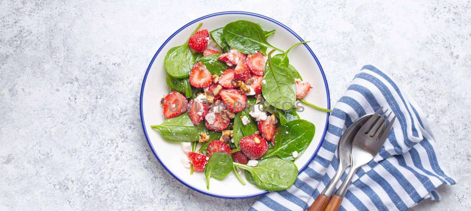 Light Healthy Summer Salad with fresh Strawberries, Spinach, Cream Cheese and Walnuts on White Ceramic Plate, white rustic stone Background Top View.