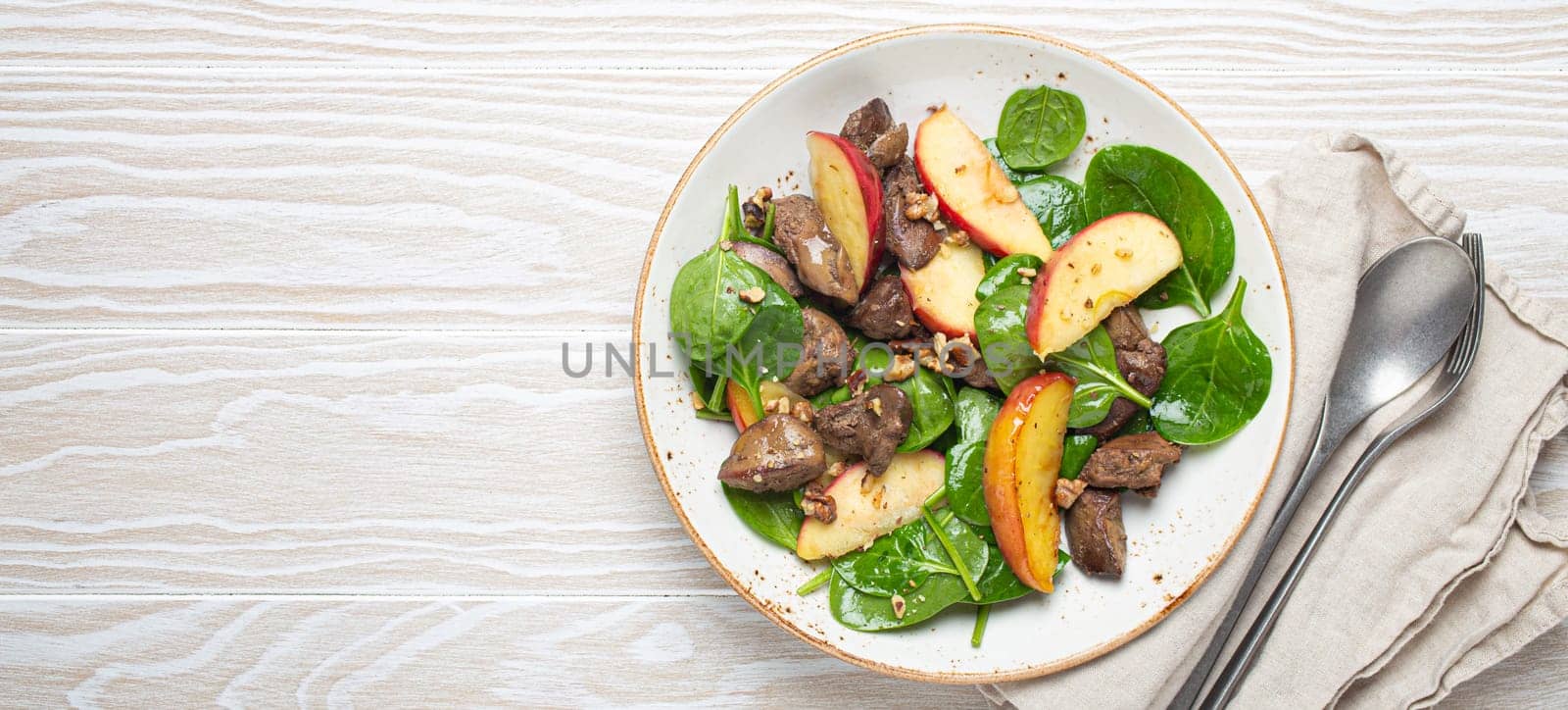 Healthy Salad with Iron Rich Ingredients Chicken Liver, Apples, Fresh Spinach and Walnuts on White Ceramic Plate, White Wooden Background From Above Space For Text.