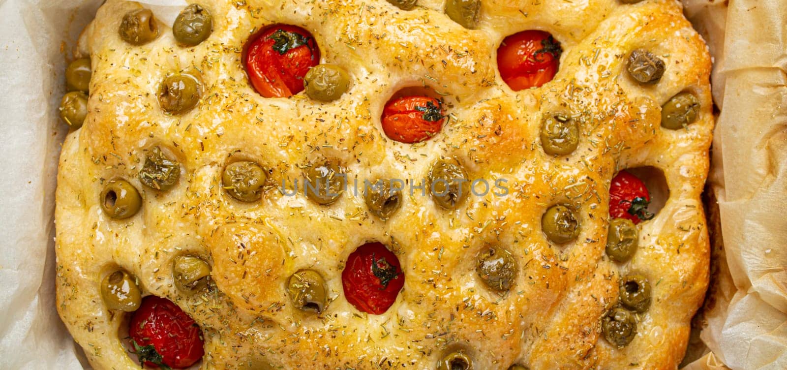 Overhead of Traditional Italian Homemade Flat Bread Focaccia with Green Olives, Olive Oil, Cherry Tomatoes and Rosemary in Baking Tray on Rustic Dark Blue Stone Background by its_al_dente