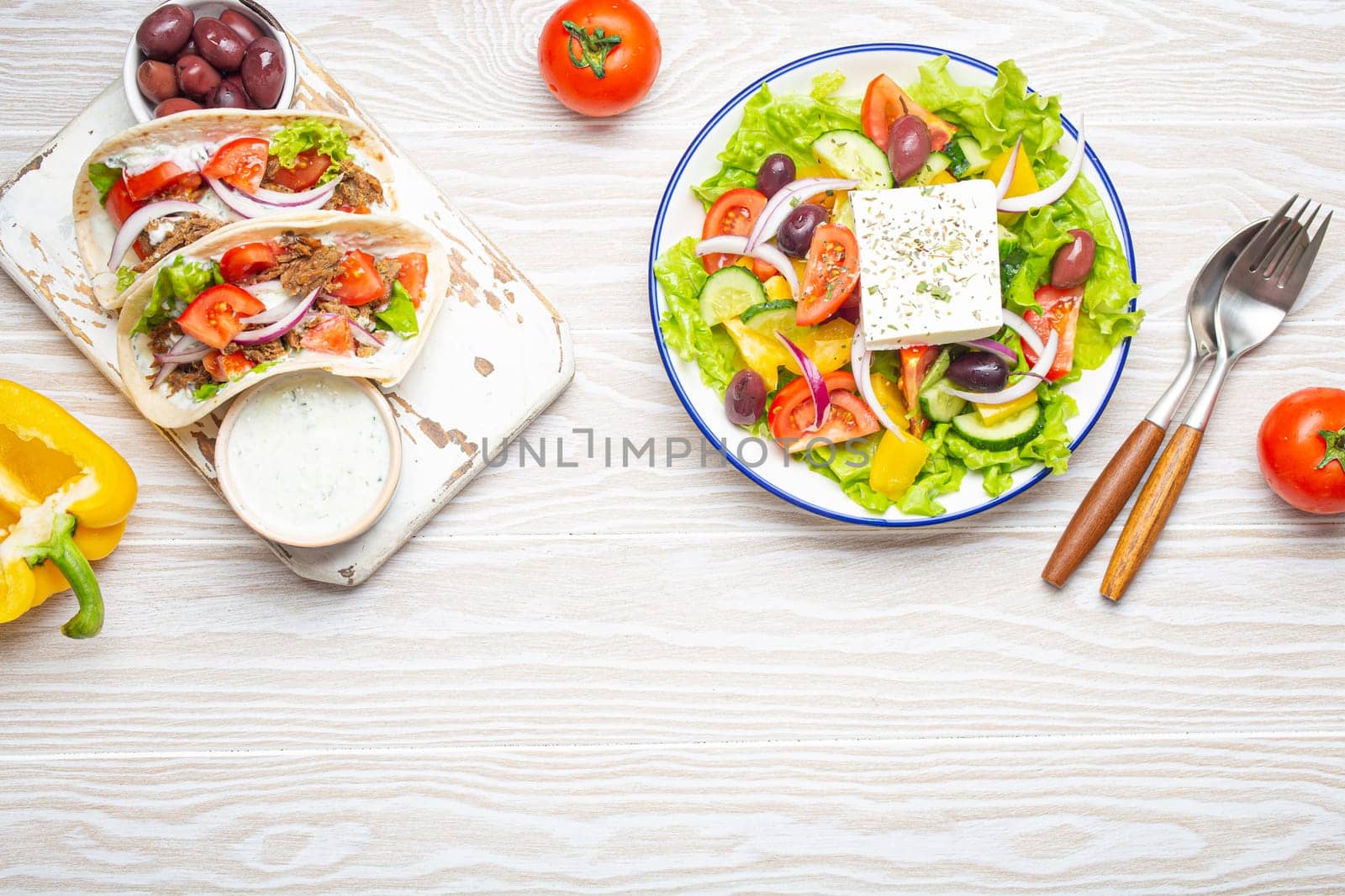 Traditional Greek Food: Greek Salad, Gyros with meat and vegetables, Tzatziki sauce, Olives on White rustic wooden table background from above. Cuisine of Greece. Copy space