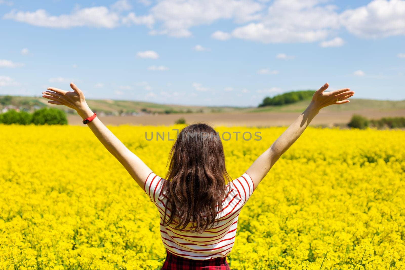 A girl stands in the middle of a beautiful rapeseed field with a beautiful blue sky. Biofuel concept