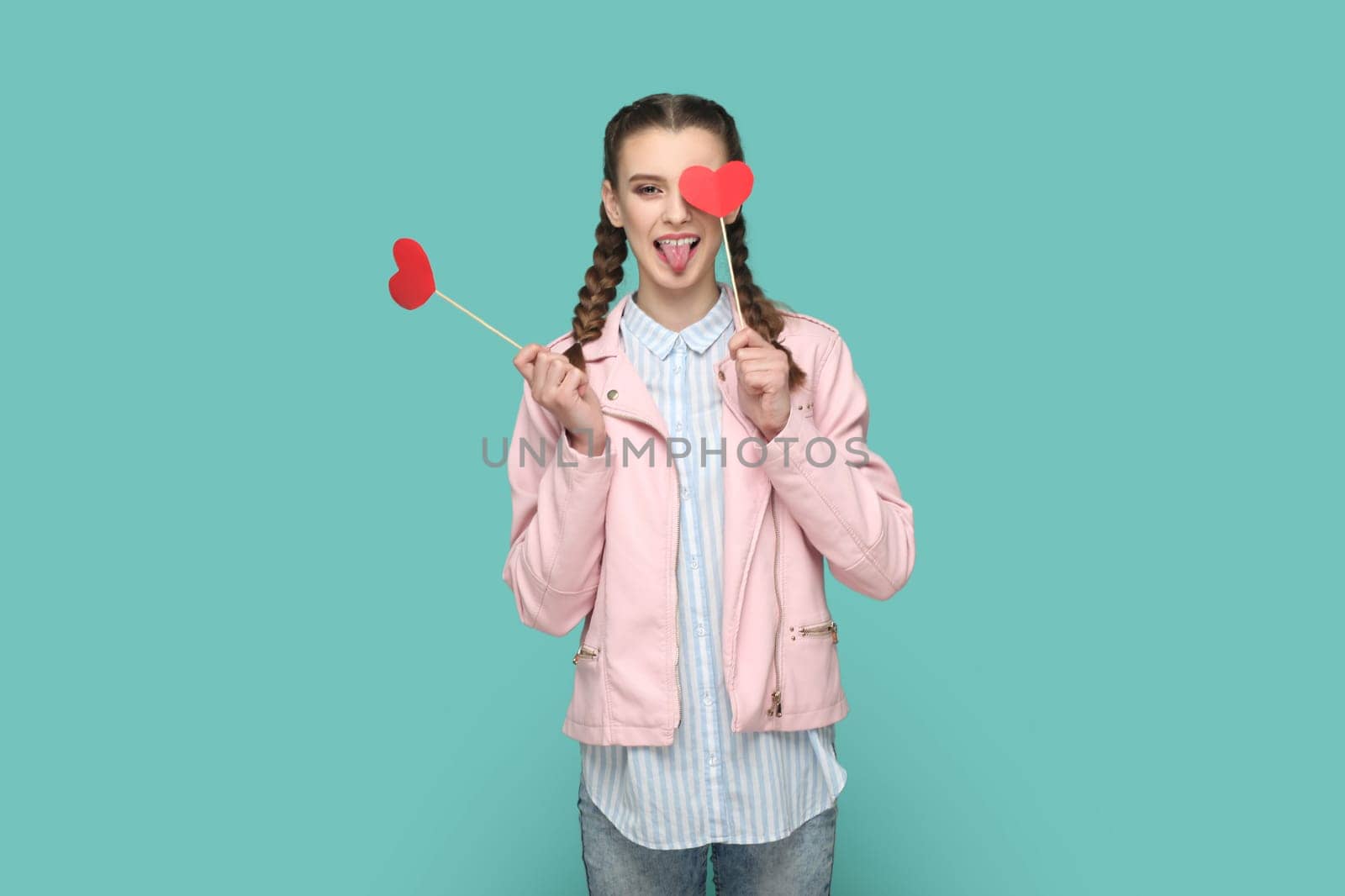 Romantic positive teenager girl standing covering eye with red heart on stick, showing tongue out. by Khosro1