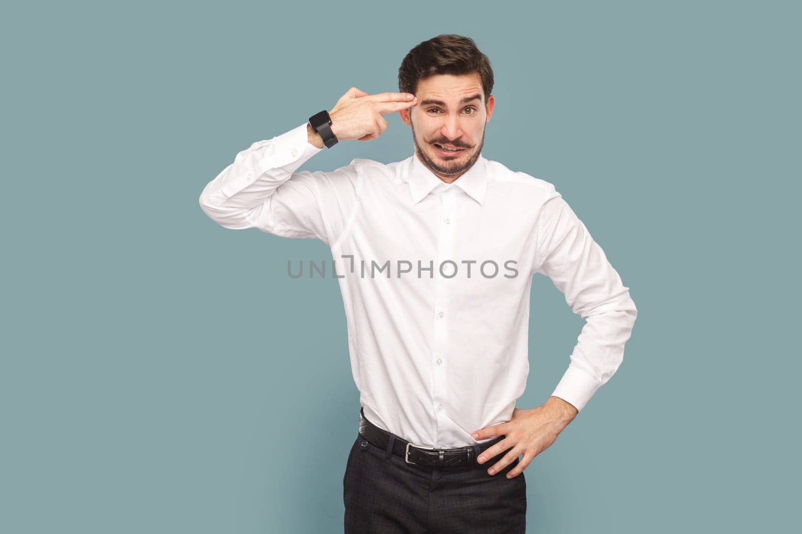 Portrait of depressed attractive man with mustache holding fingers gun near his temple, being in bad mood and stress, wearing Indoor studio shot isolated on light blue background.