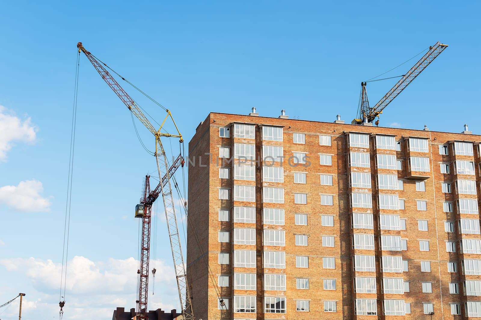 The construction of a new apartment building, against the background of the blue sky, a high-rise construction crane