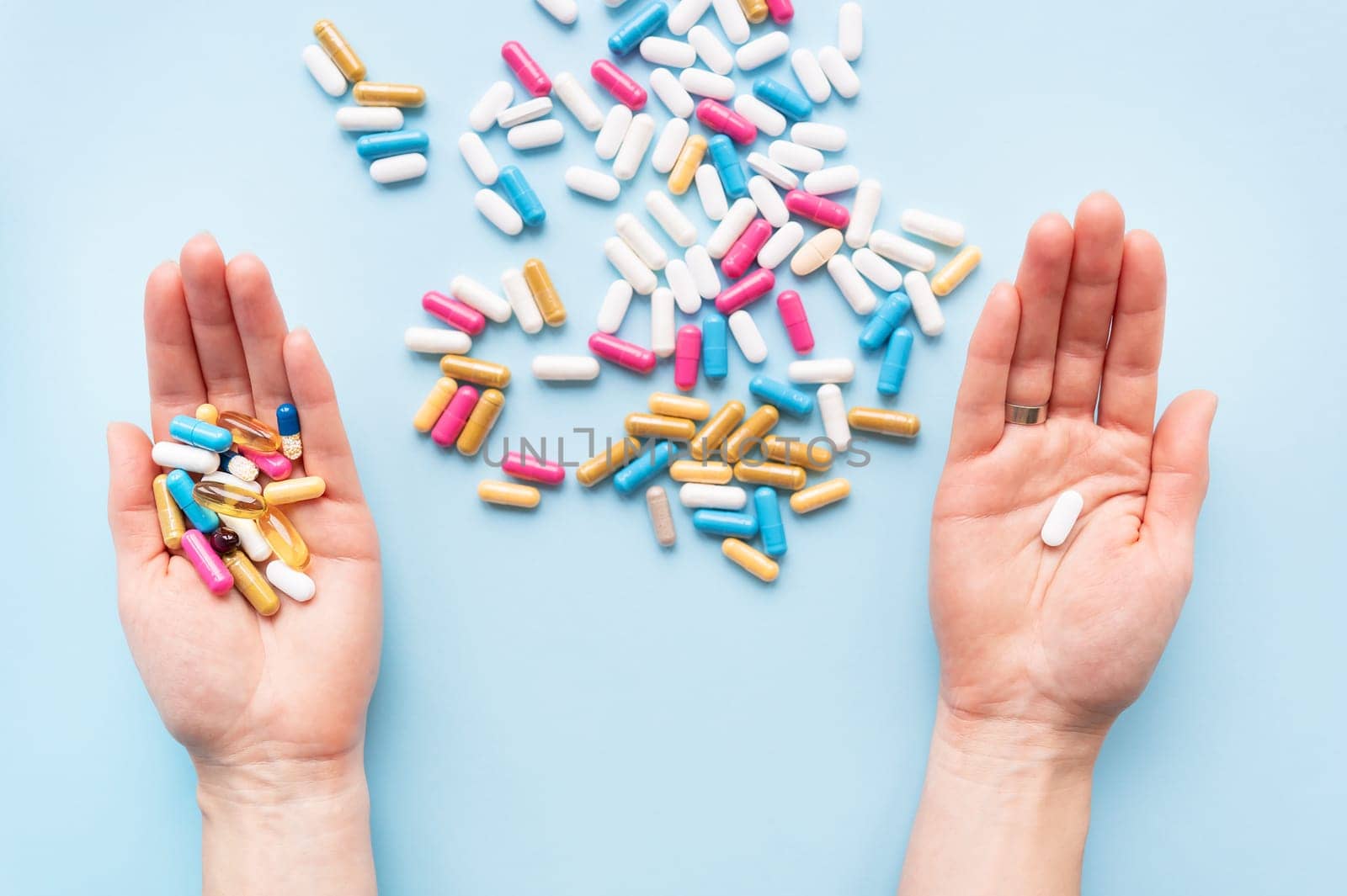 The girl holds a handful of bright vitamins in her hands, and one pill in the other, food supplements and medicines on a blue background. Concept of medicine and healthcare