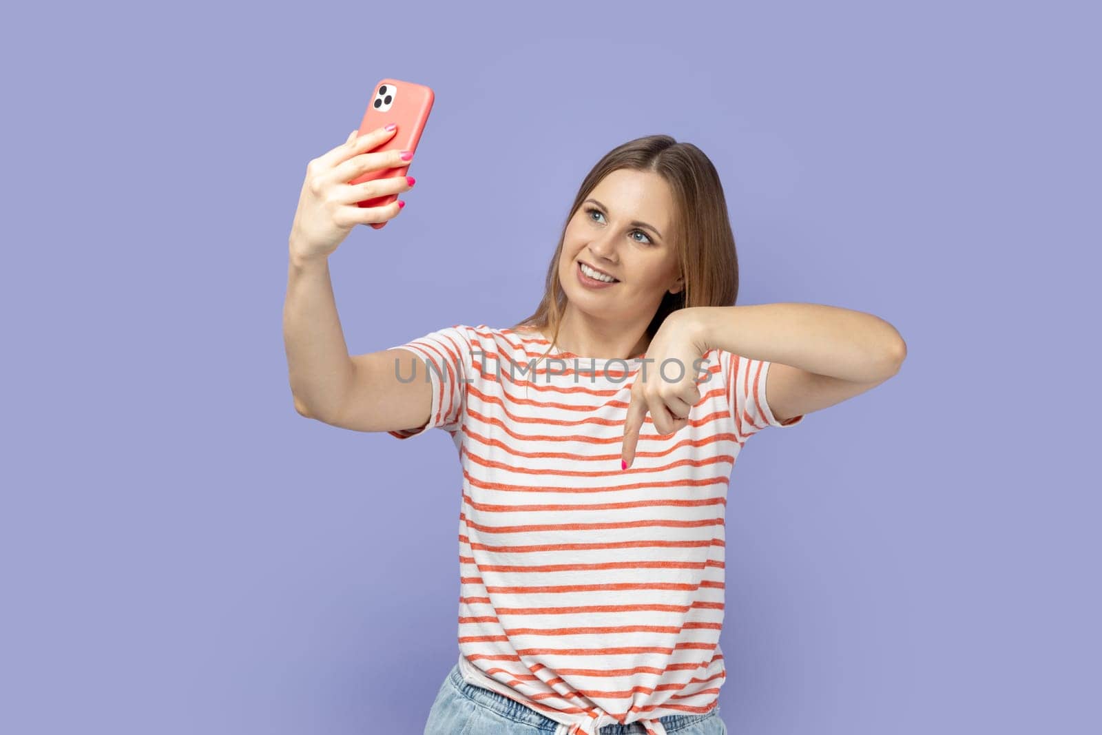 Woman standing with mobile phone and broadcasting livestream, pointing down, asking to subscribe. by Khosro1