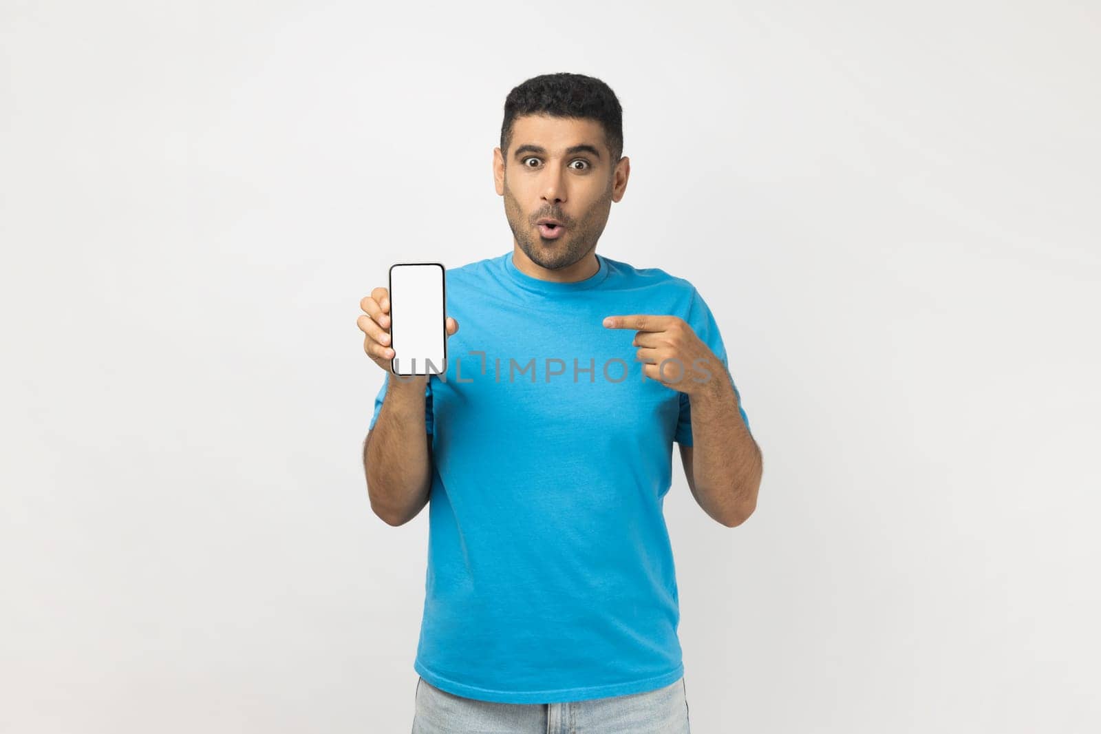 Shocked amazed man pointing at smart phone with blank white display, mockup for promotional text. by Khosro1