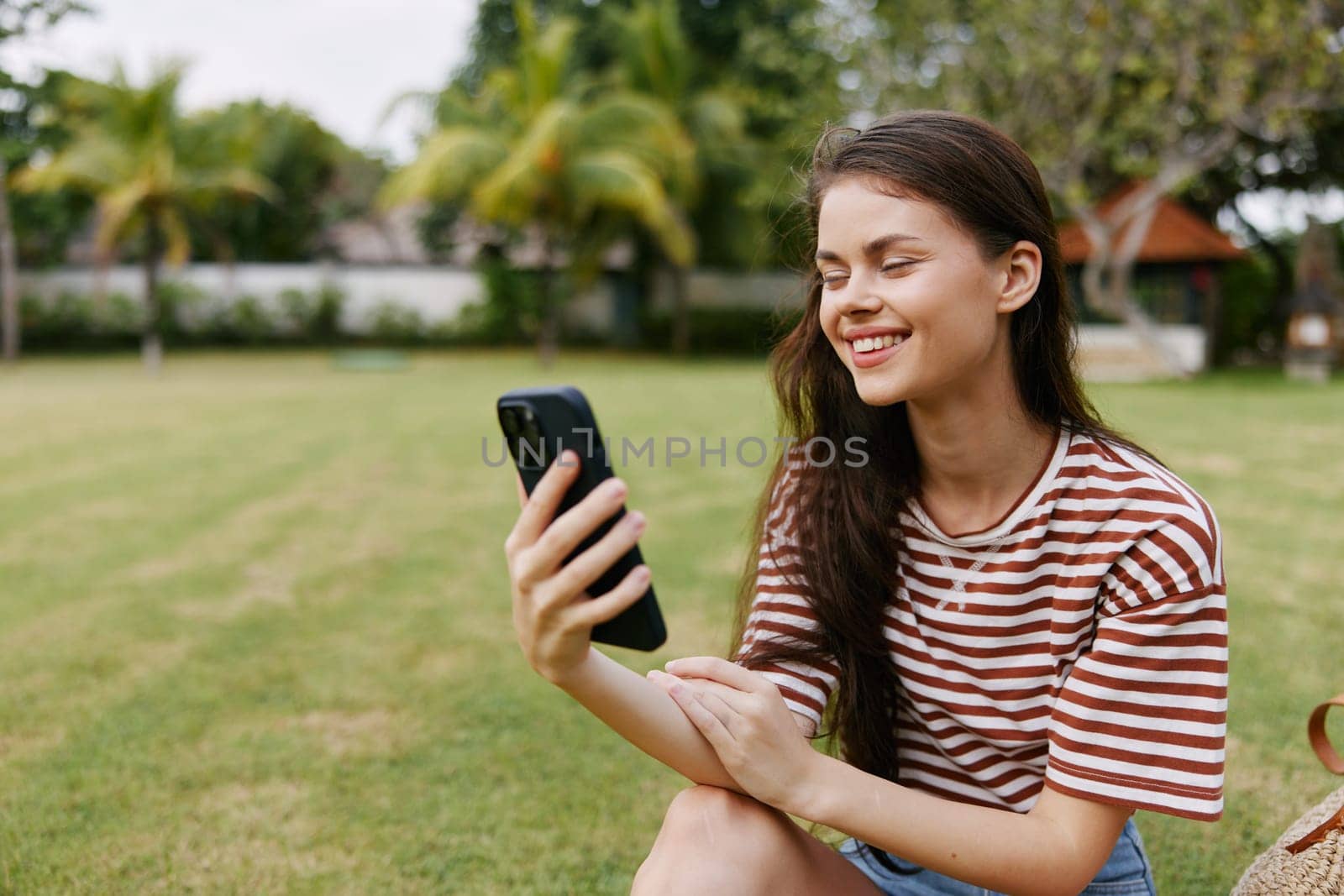 woman blogger happy smartphone network park call shirt cellphone mobile grass smiling female striped outside nature tree lifestyle walk phone palm caucasian