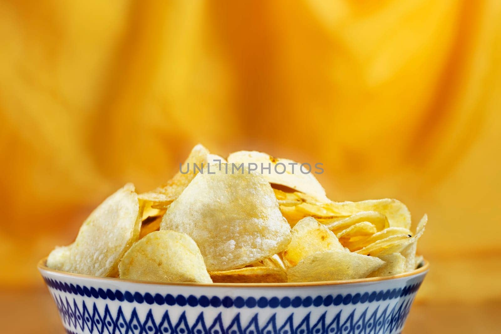 Potato chips  in colored  bowl against yellow background ,party time